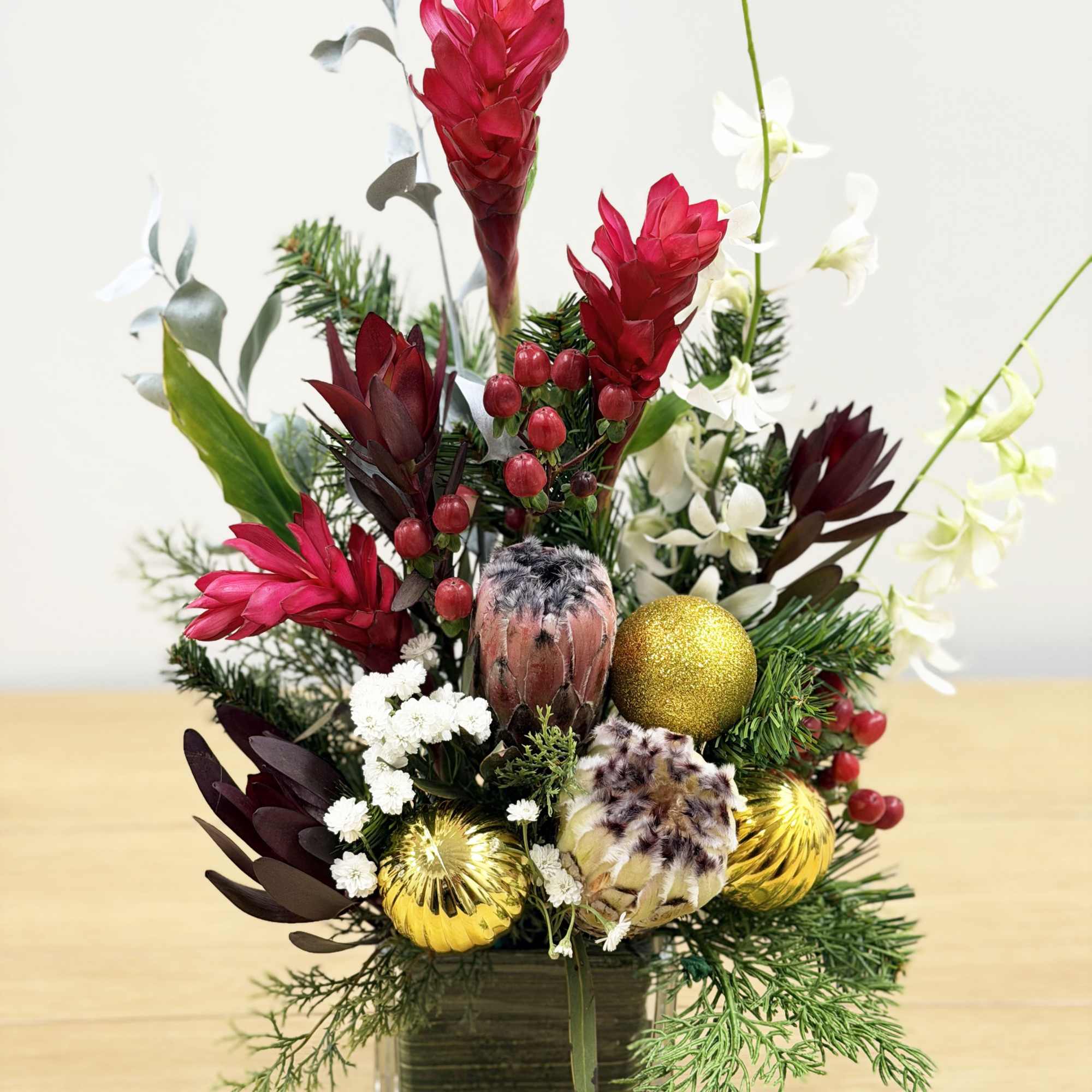 Tropical floral arrangement in a square glass vase with red blooms and gold ornaments