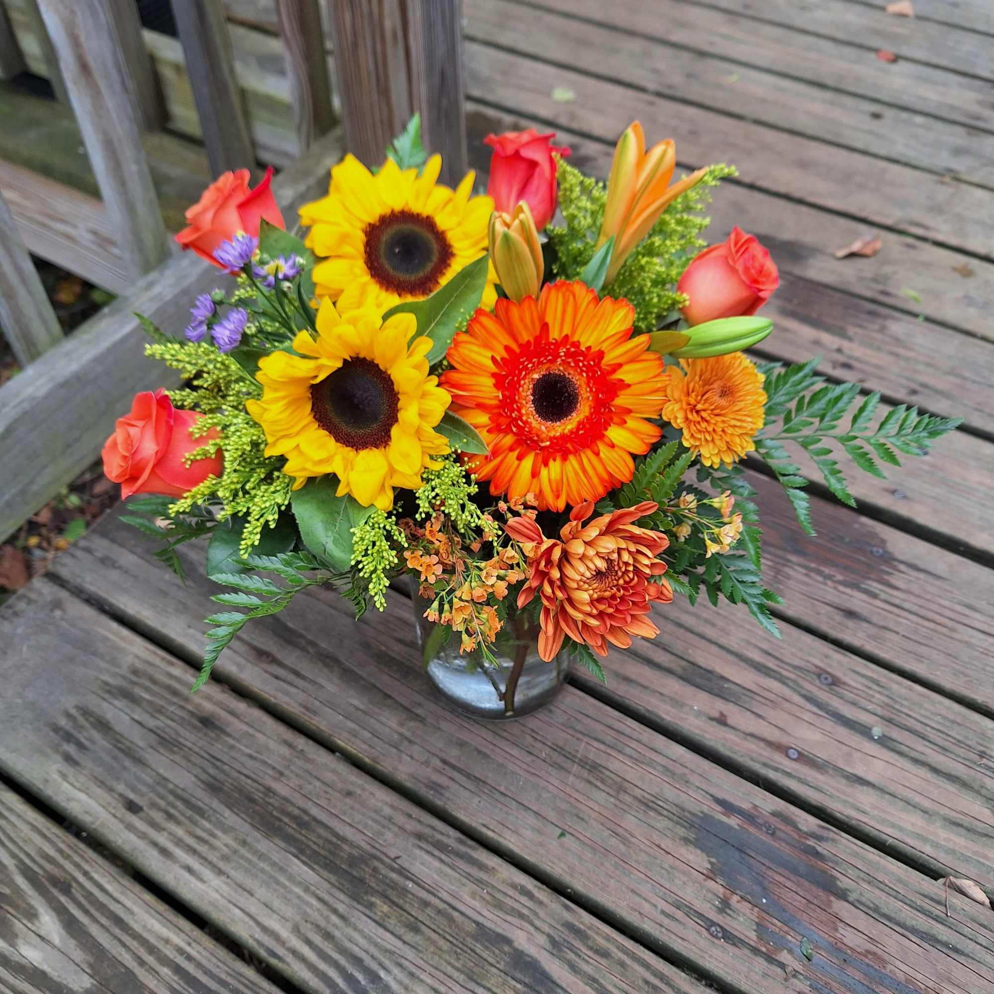 Mixed bouquet with sunflowers, roses, and orange blooms in a glass vase