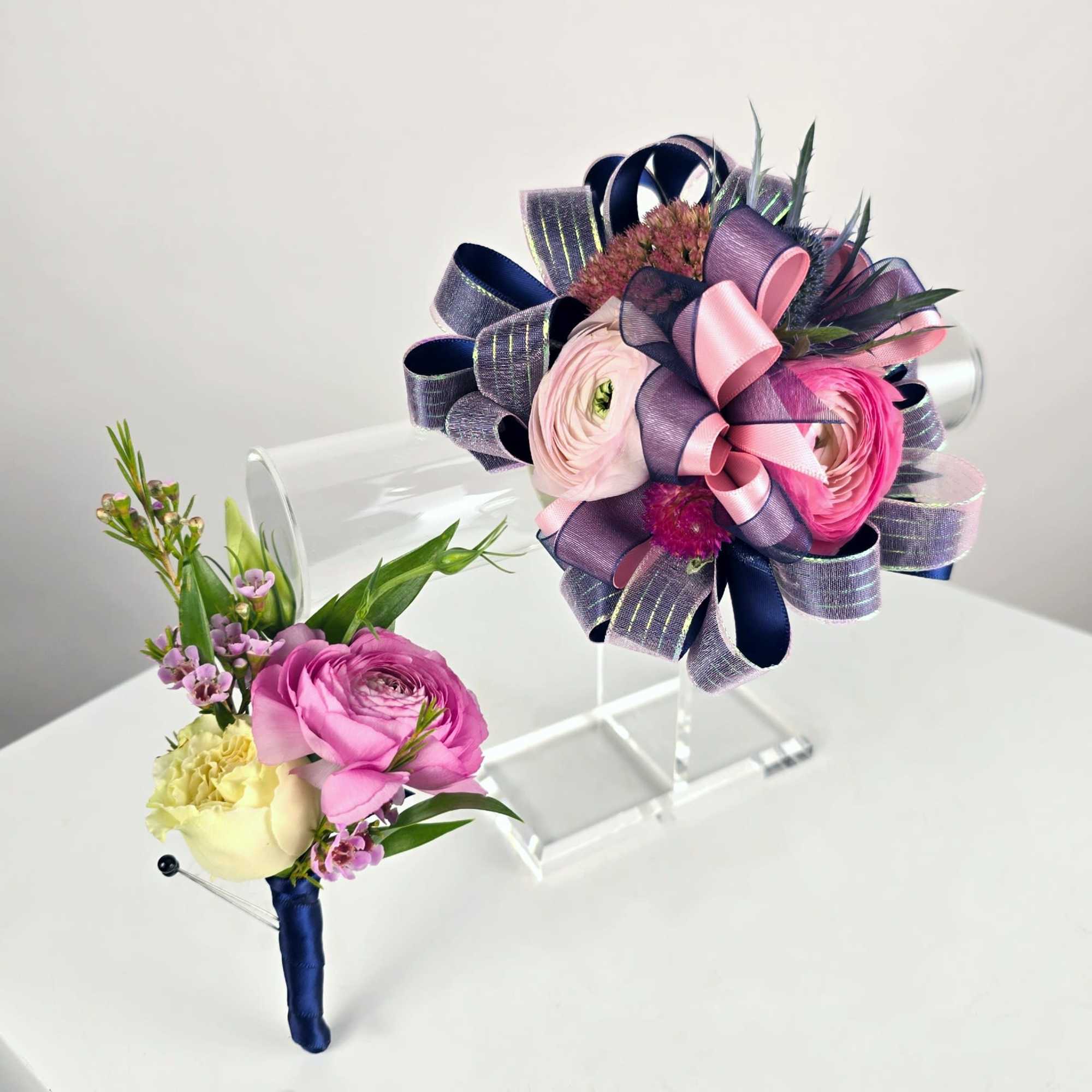 Two floral boutonnieres with pink and cream blooms and ribbon accents