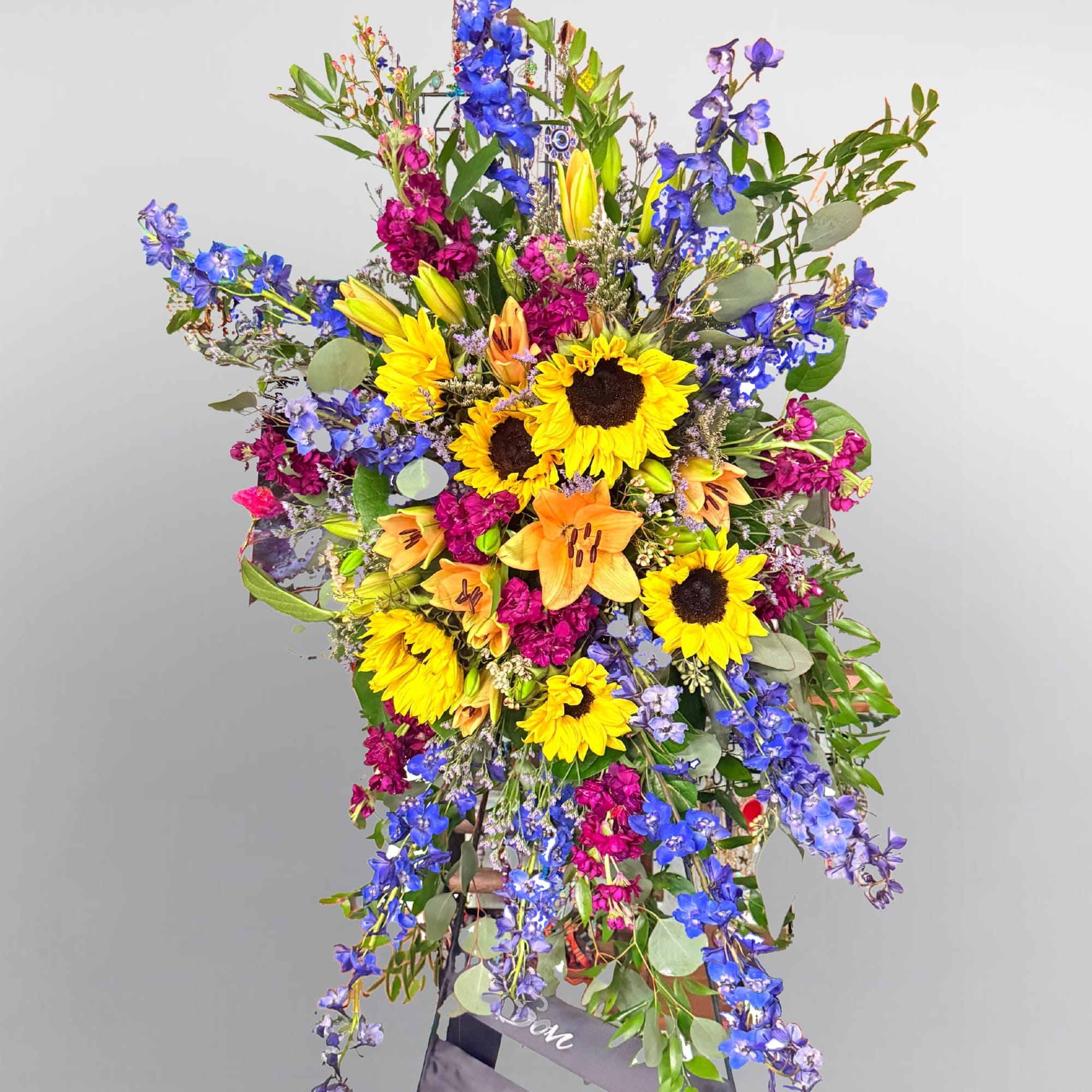 Tall floral standing spray with sunflowers, lilies, and blue delphinium