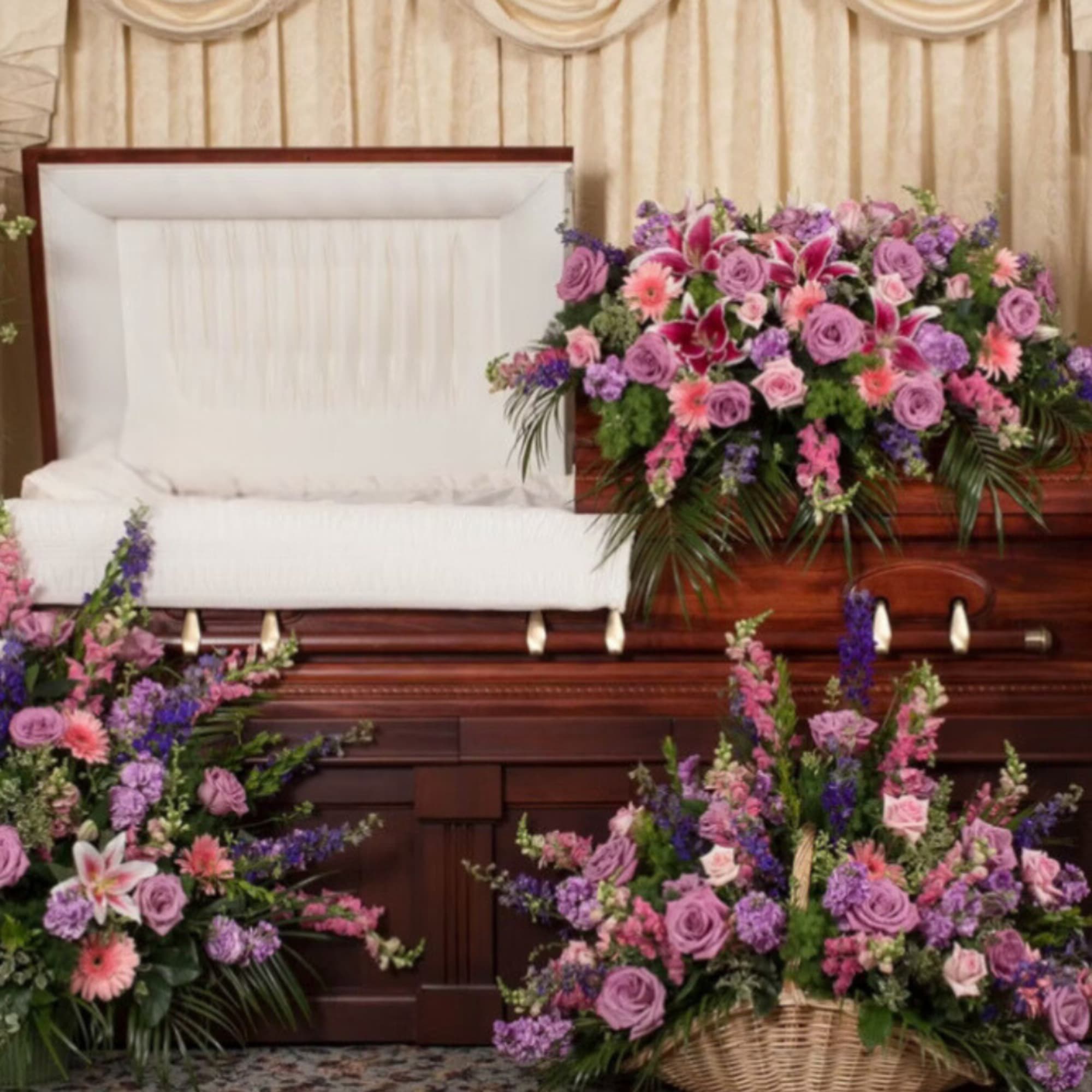 Funeral casket surrounded by purple and pink floral sprays and wreaths
