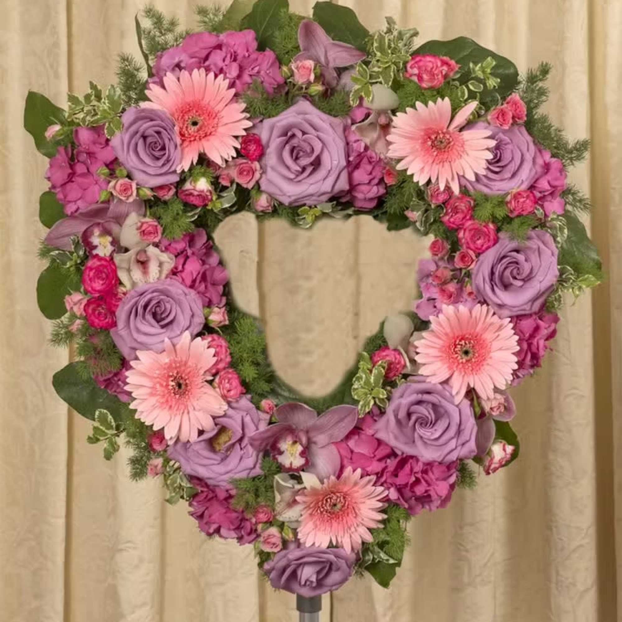 Heart-shaped floral wreath with pink and lavender flowers on a stand