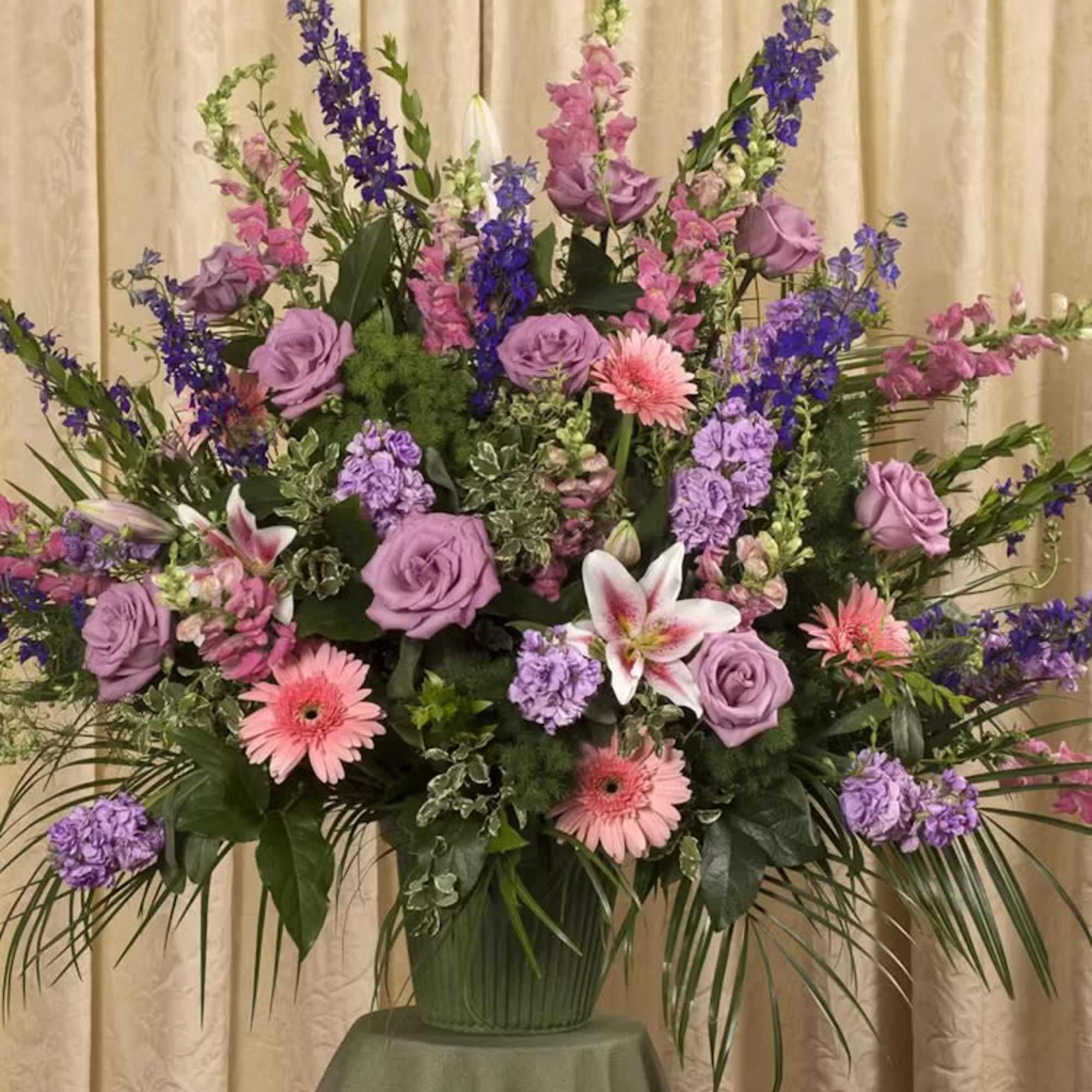 Large floral arrangement with lavender roses, pink gerberas, and purple spikes in a vase.