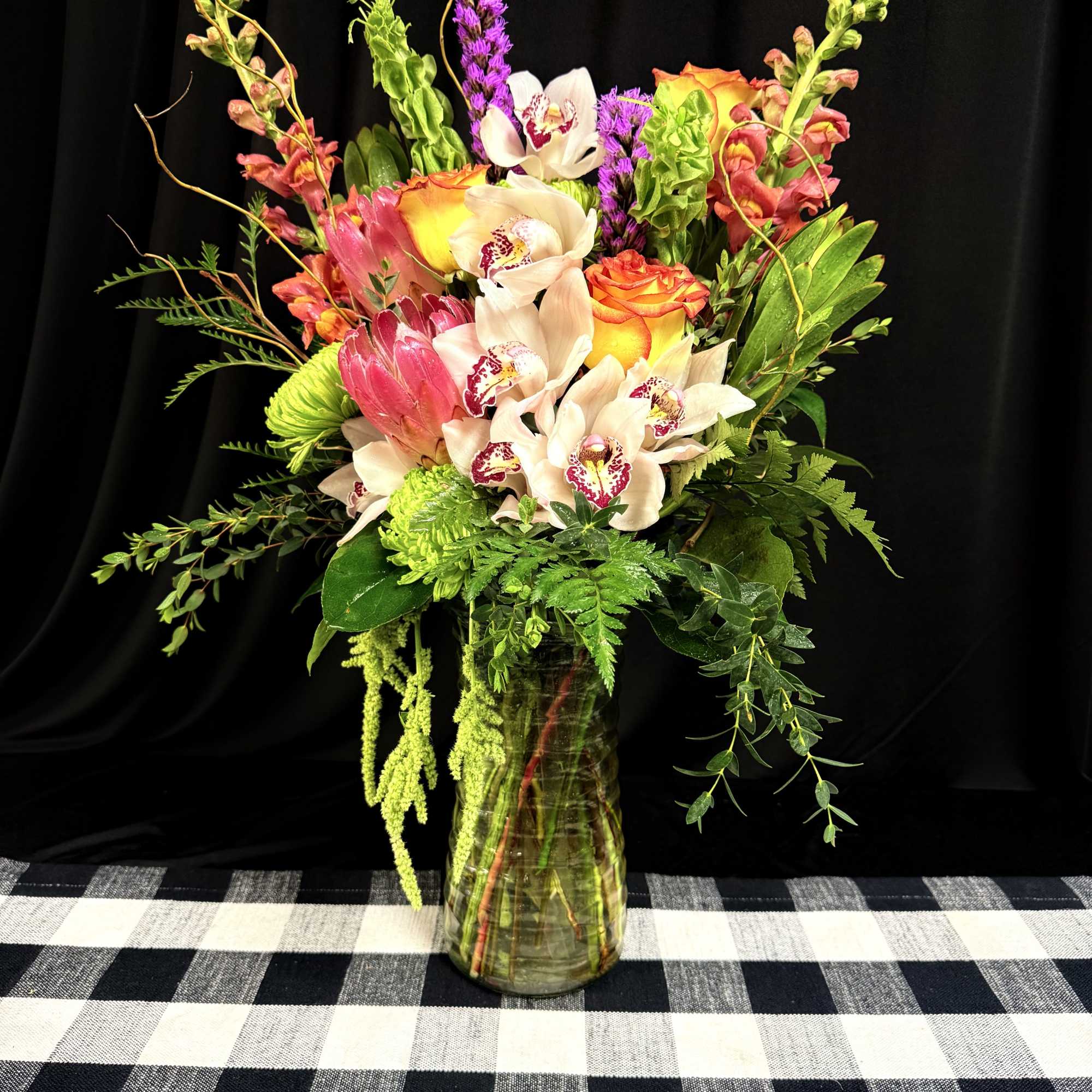 Mixed bouquet of orchids, roses, and tropical flowers in a glass vase