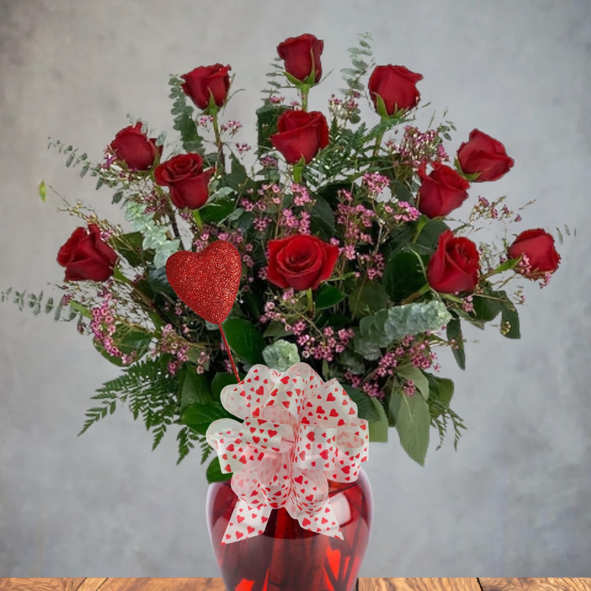 Red roses in a red glass vase with a heart-patterned bow and balloon
