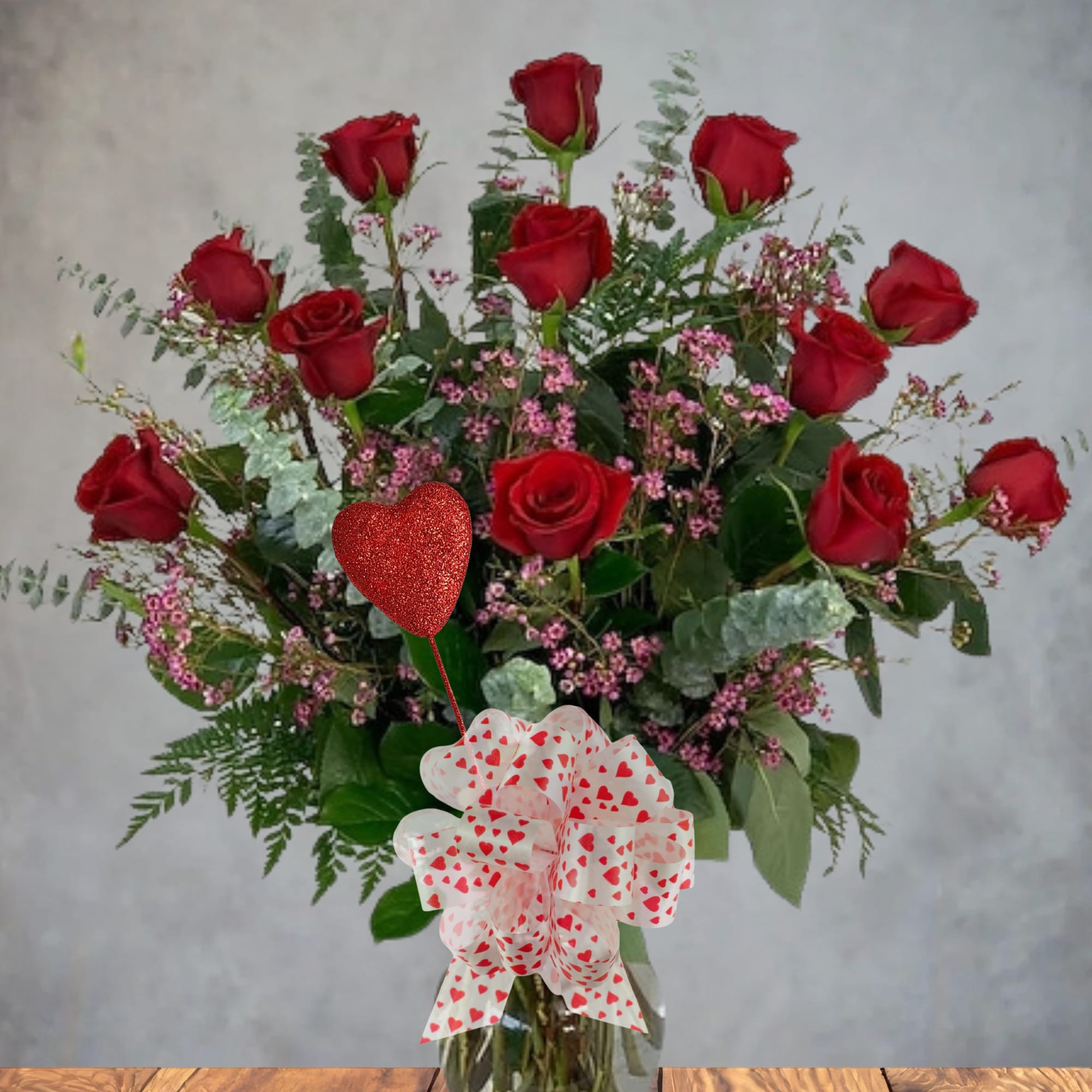 Red roses in a glass vase with a heart balloon and heart-patterned bow