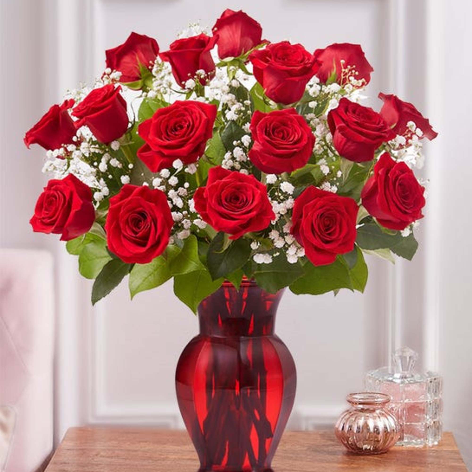 Red roses arranged in a red glass vase with white baby's breath