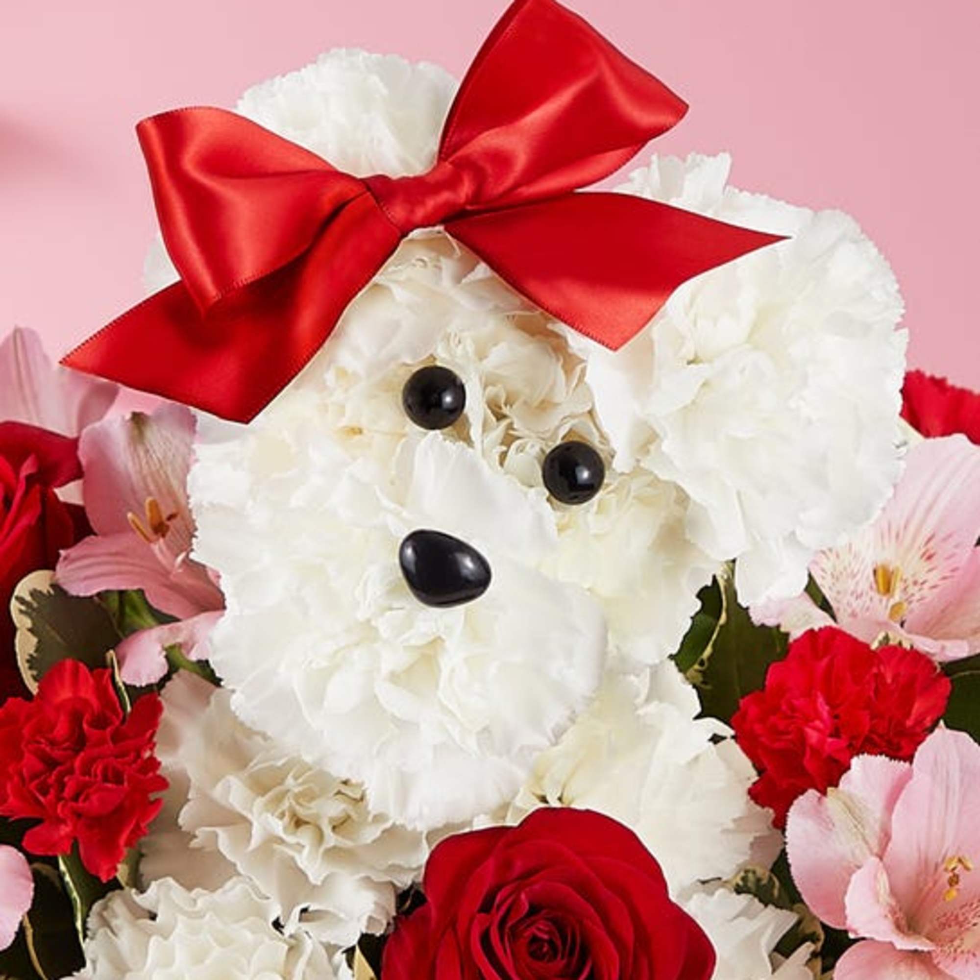 White teddy bear made of flowers with a red bow, surrounded by pink and red blooms