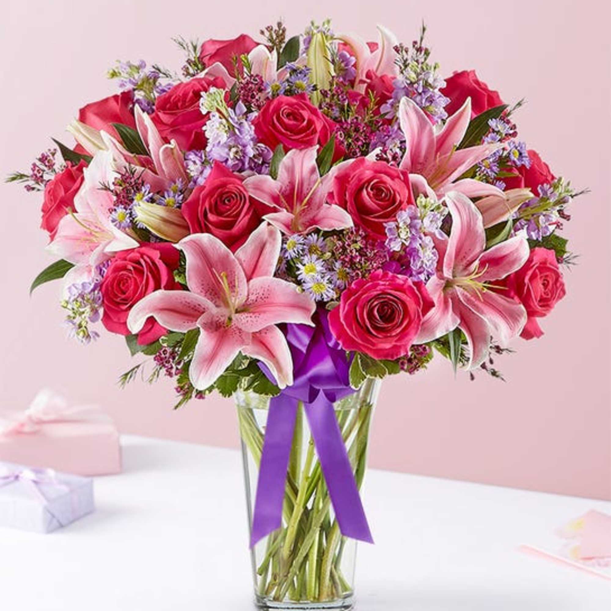 Bouquet of pink roses and lilies in a clear glass vase with a purple ribbon