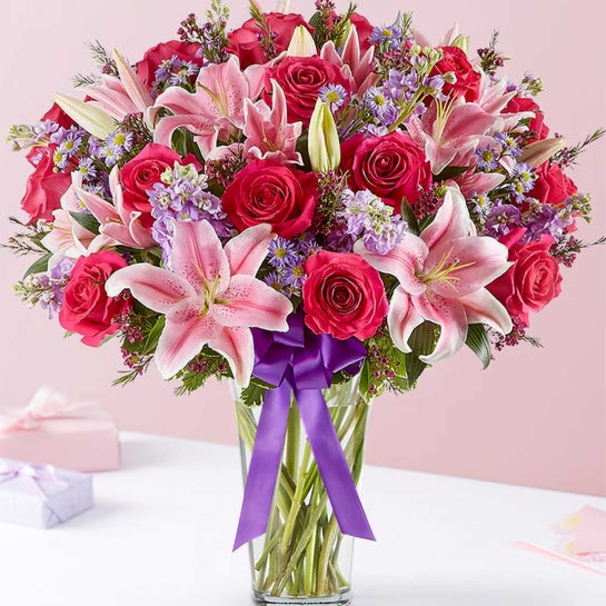 Pink roses and lilies in a clear glass vase with a purple ribbon