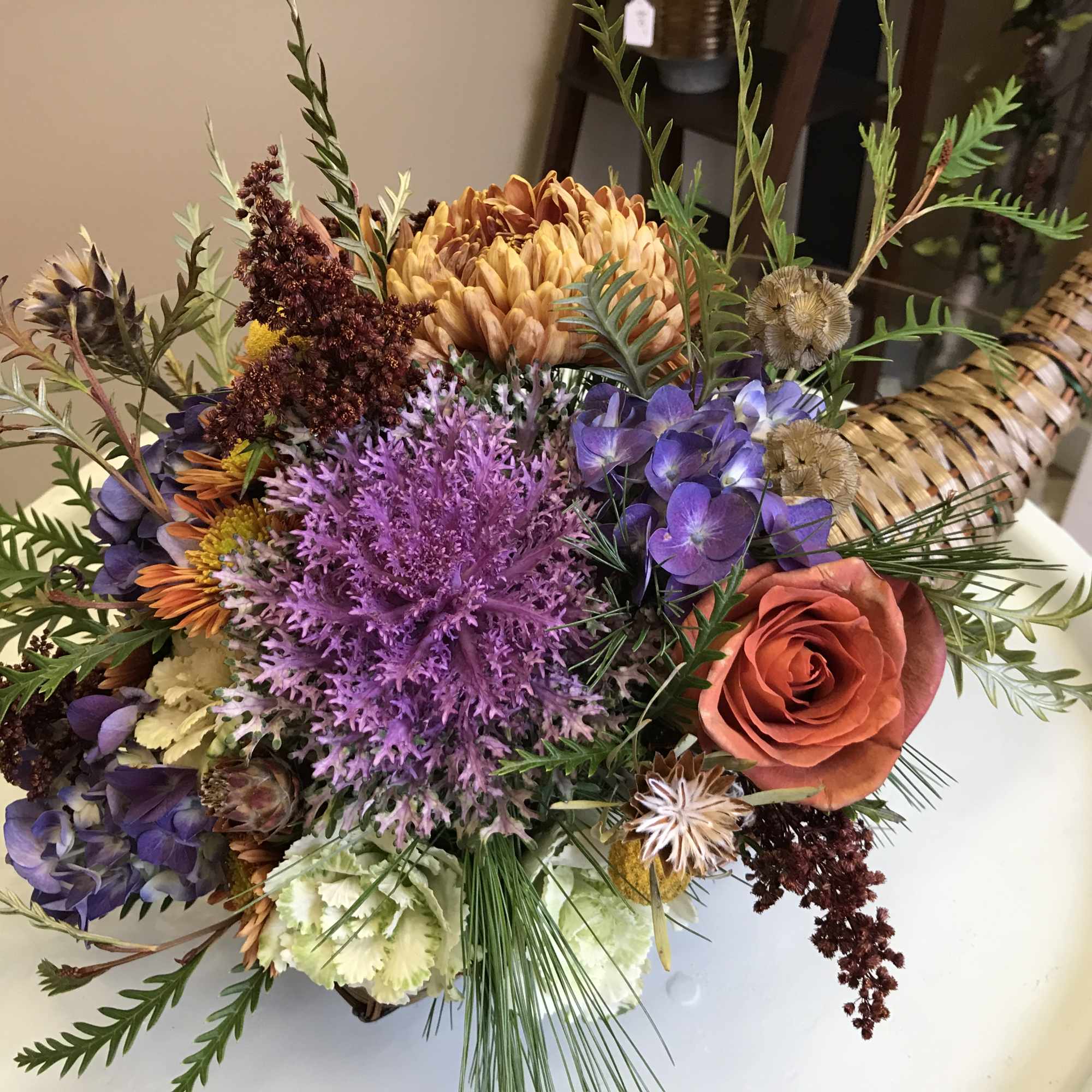 Mixed bouquet with purple, orange, and coral flowers in a woven basket