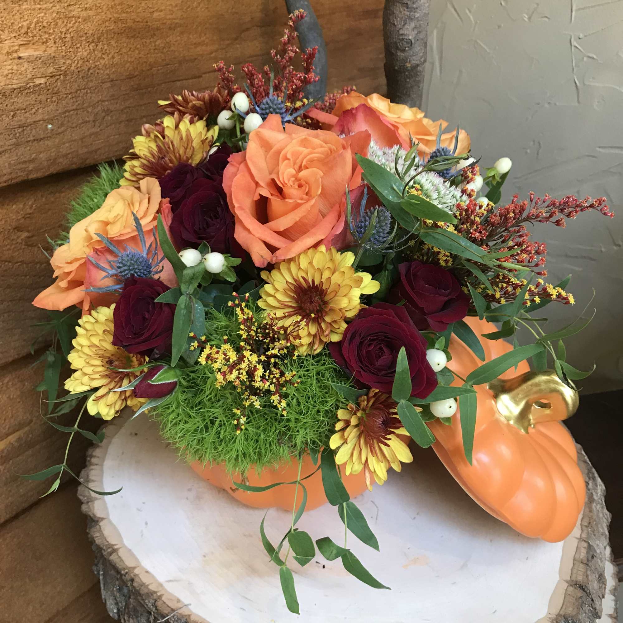 Orange and burgundy floral arrangement in a pumpkin container
