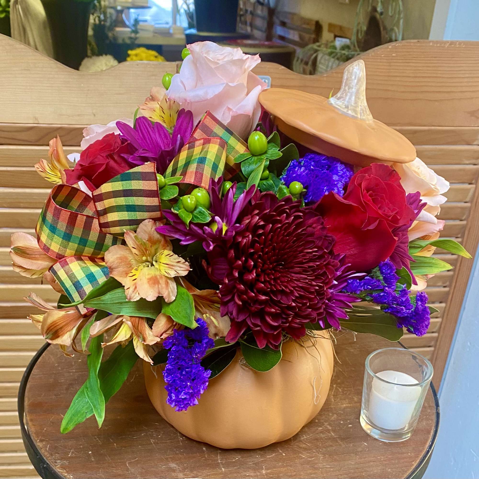 Floral arrangement in a pumpkin-shaped container with a plaid ribbon and candle beside it