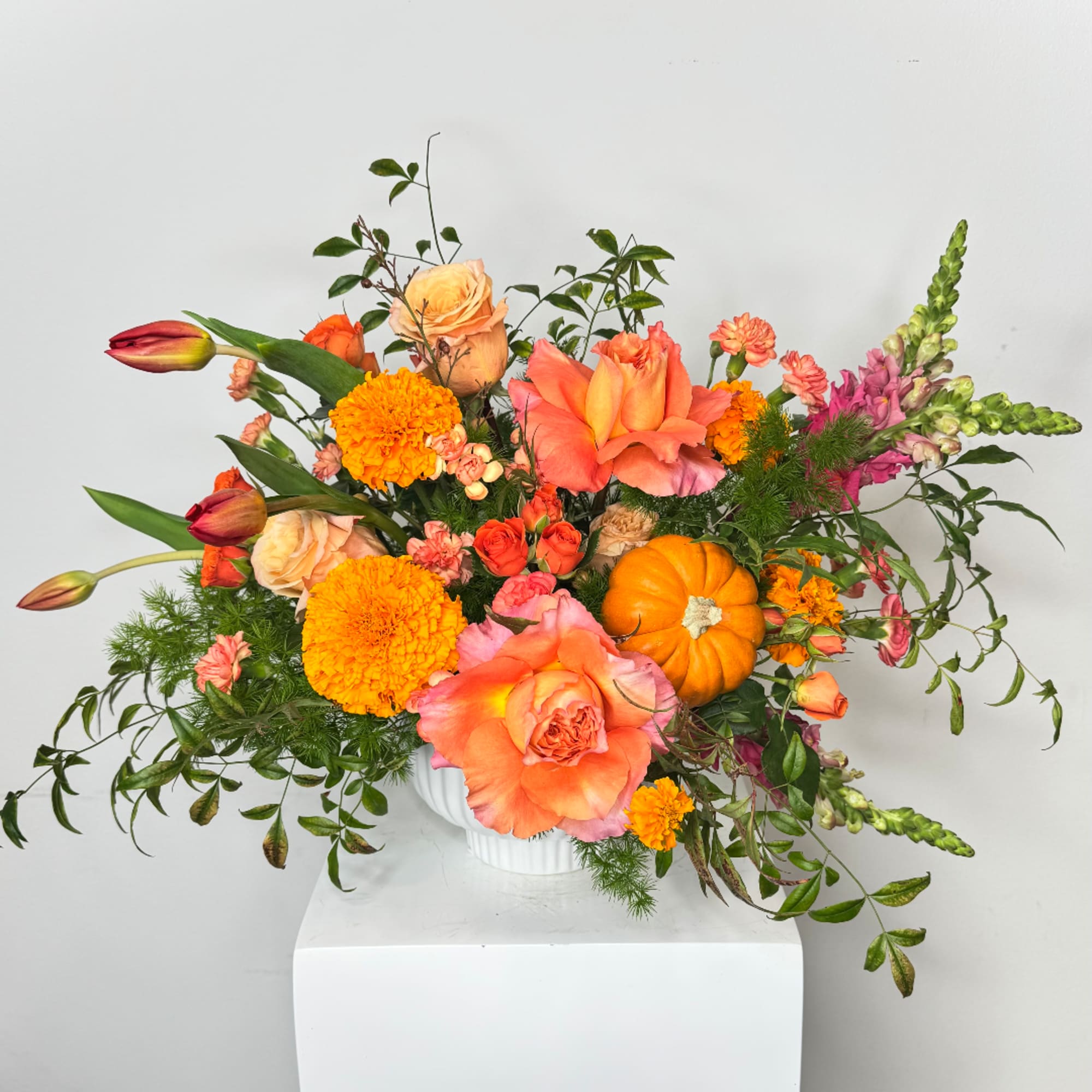Orange and pink floral arrangement in a white vase with marigolds and roses