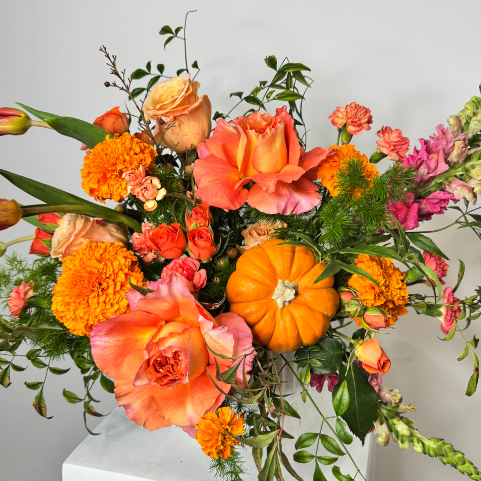 Orange roses and marigolds arranged with a small pumpkin in a vase.