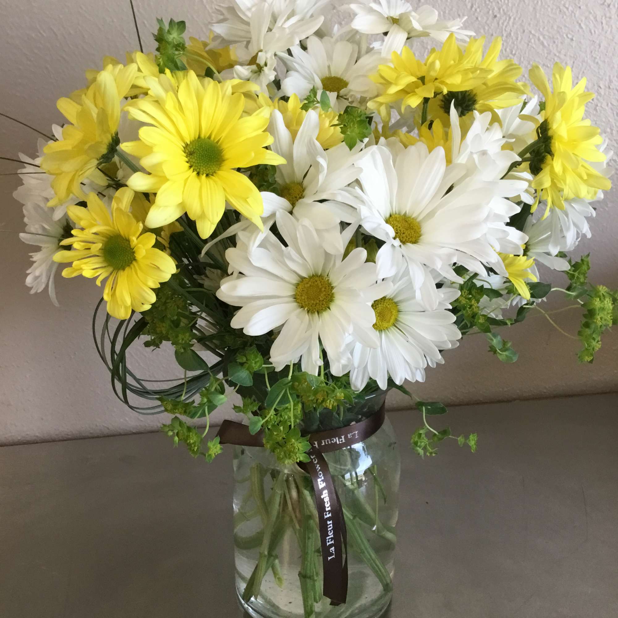 Overflowing with daisies (color may vary) and accompanying greenery/filler