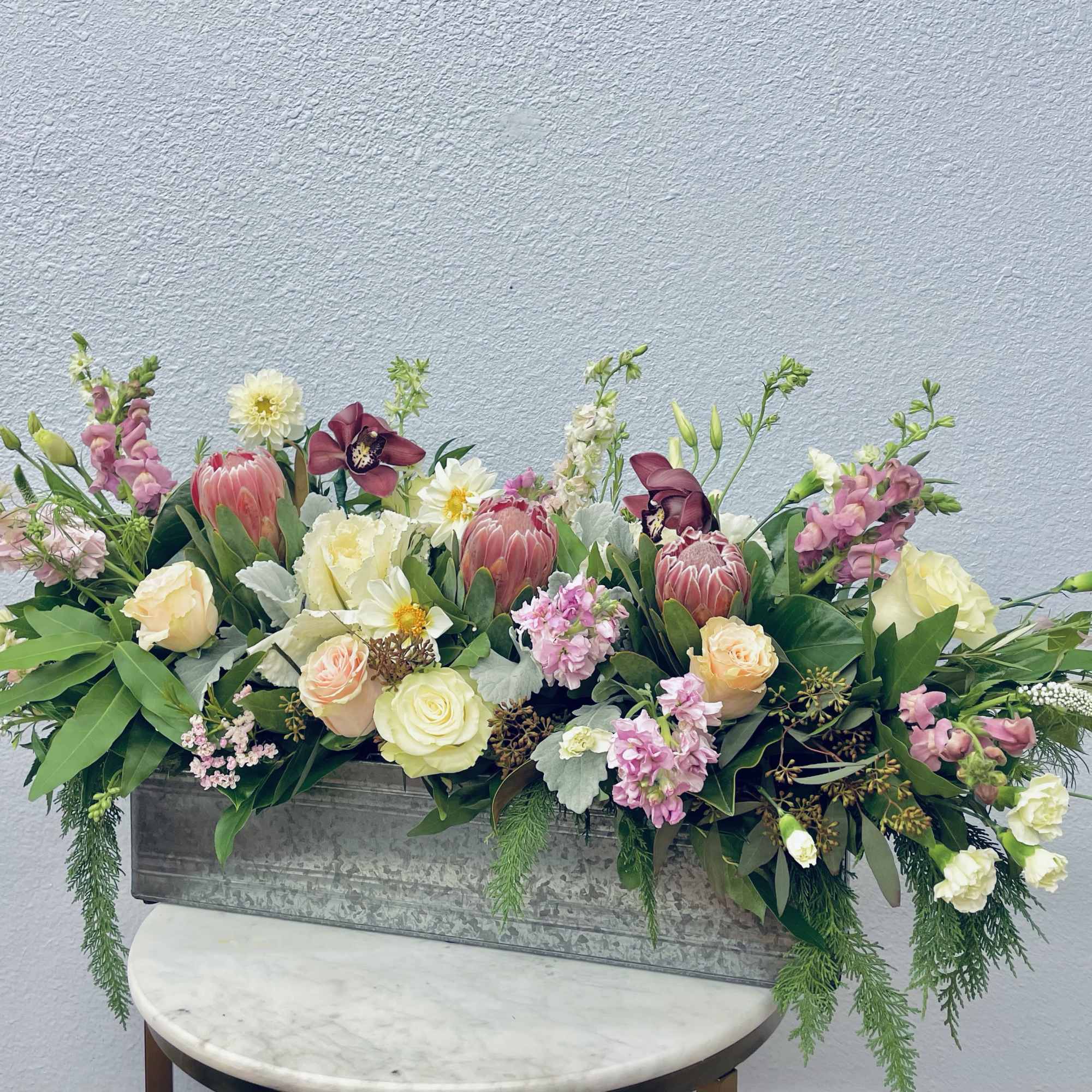 Long floral arrangement in a metal container with pink, cream, and white blooms