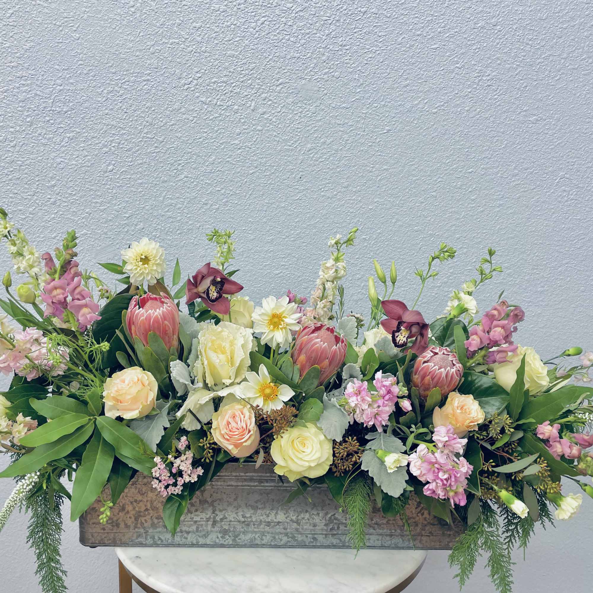 Long floral centerpiece in a rectangular metal container with pink, cream, and white blooms