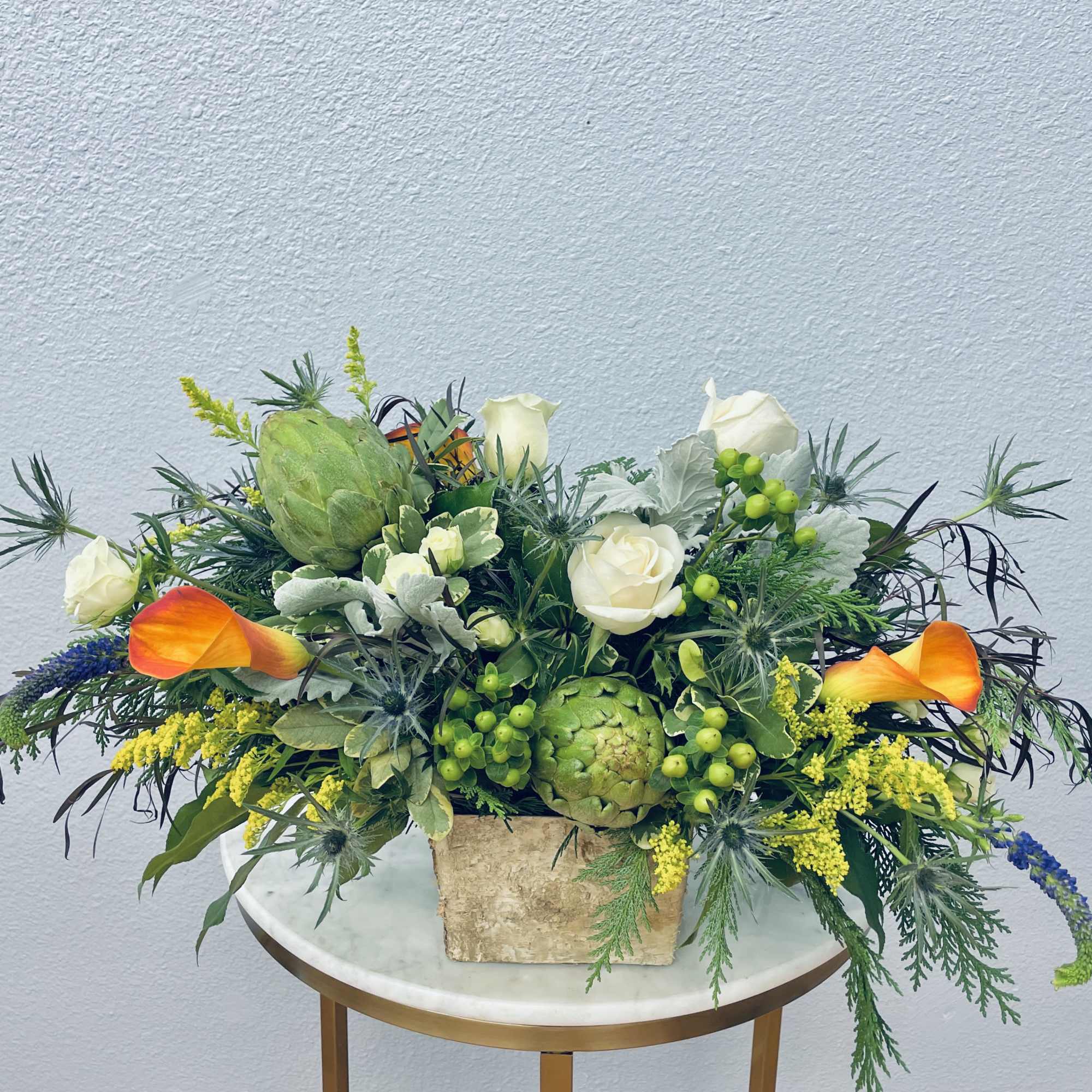 Mixed floral arrangement in a square stone vase with white roses and orange calla lilies