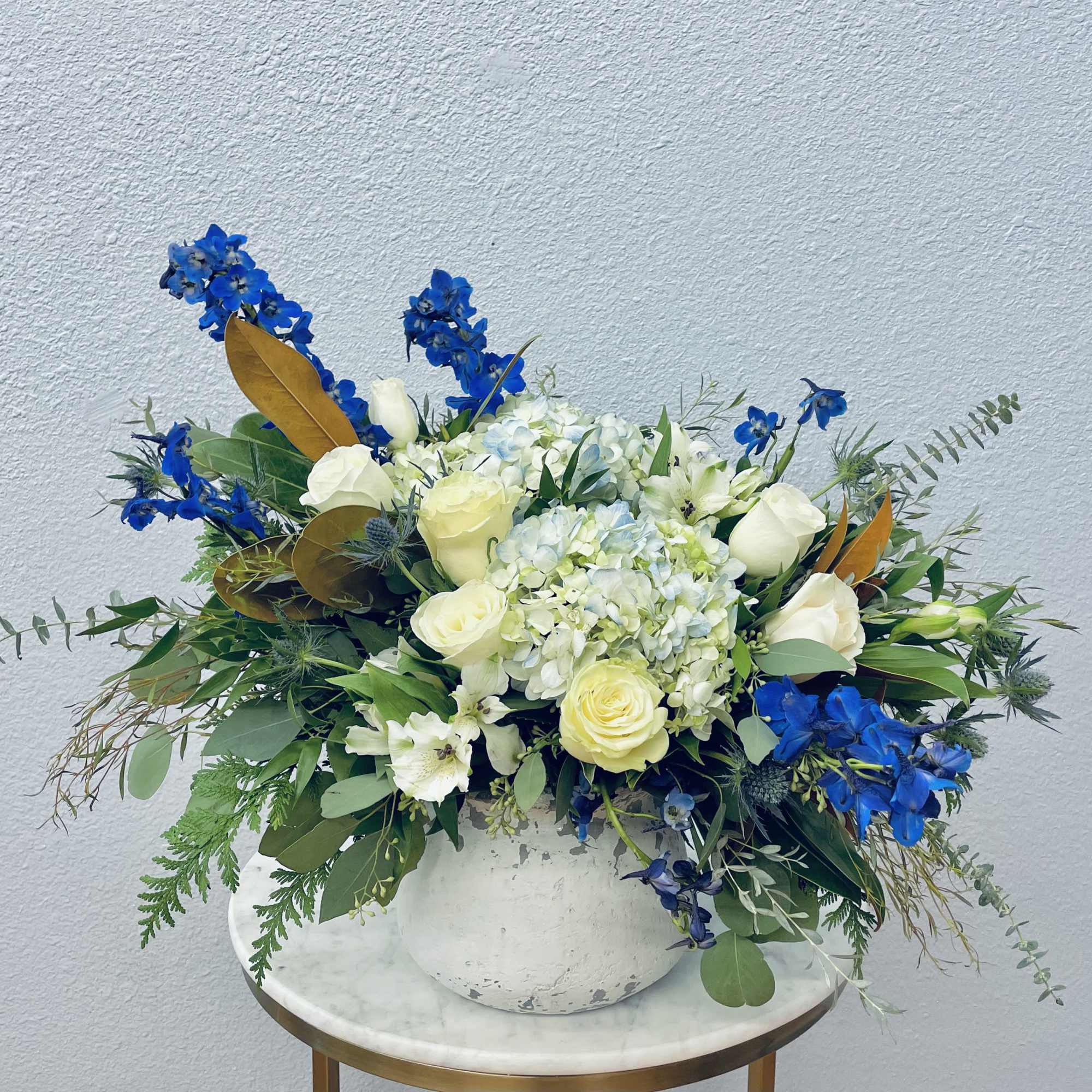 White and pale yellow roses with blue flowers in a white vase