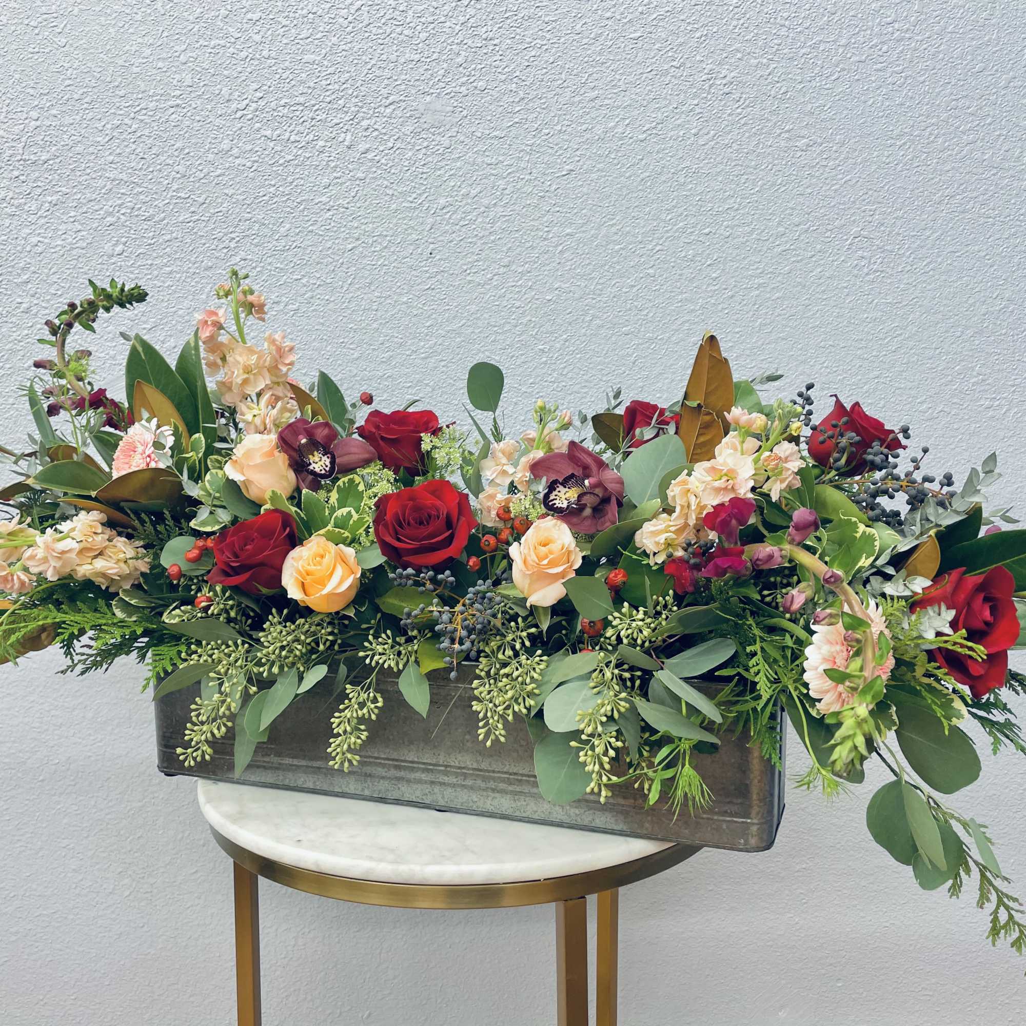 Long rectangular floral arrangement with red and peach roses in a low vase