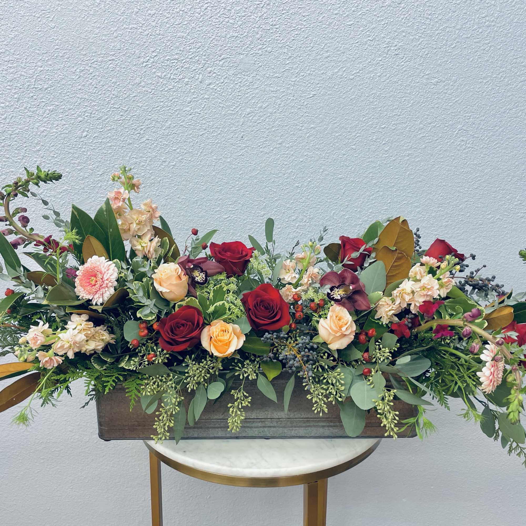 Long floral arrangement with red and peach roses in a rectangular container