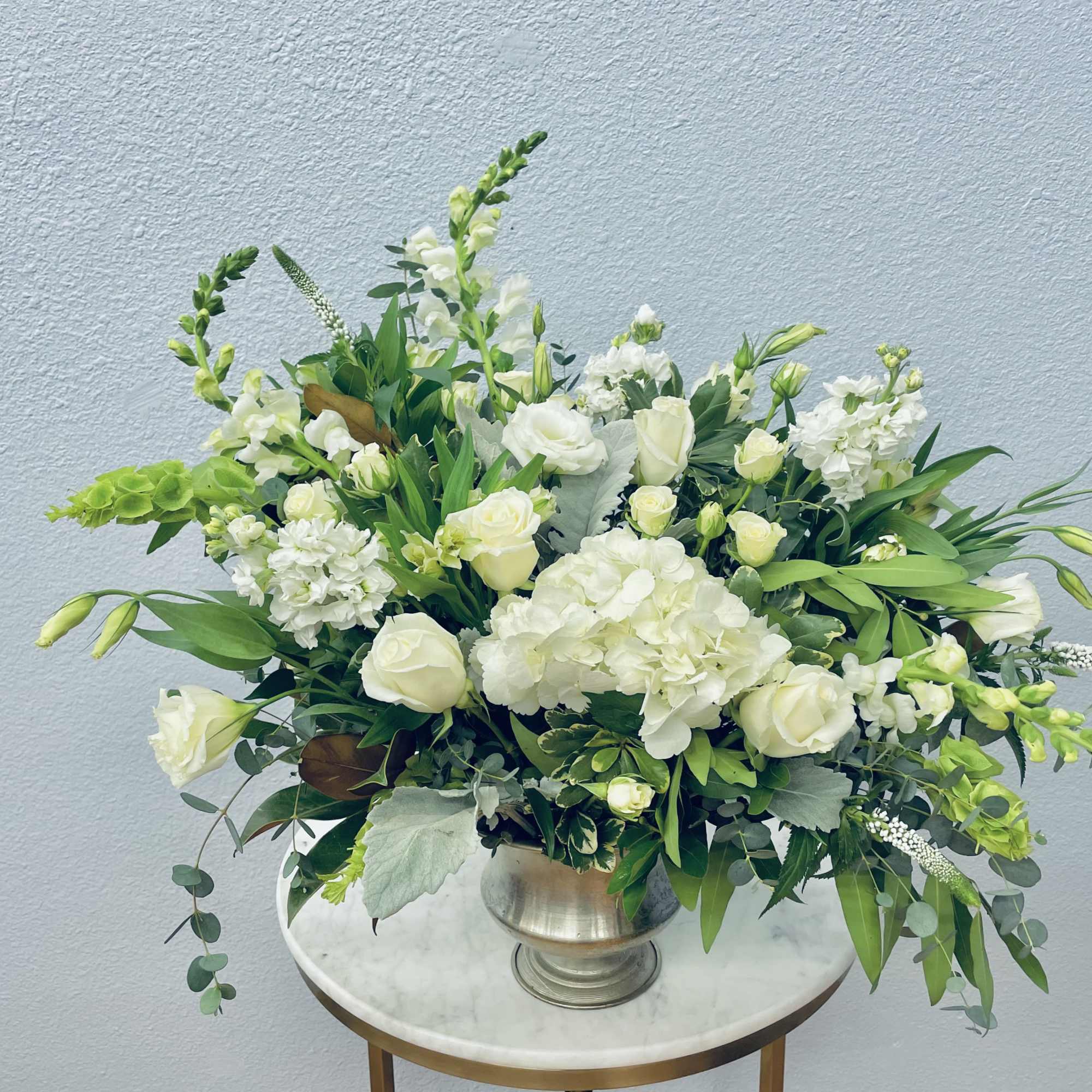 White floral arrangement in a silver vase with green accents
