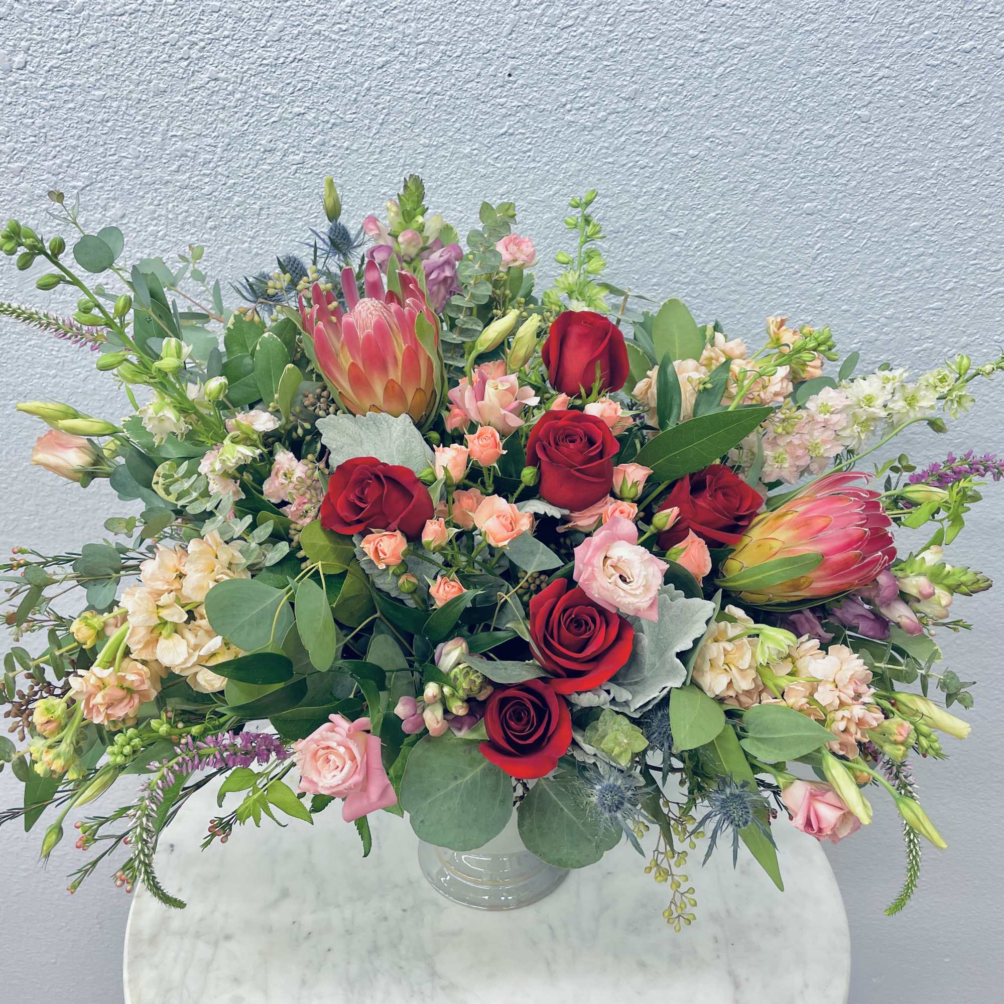 Mixed bouquet of red roses and pink blooms in a clear glass vase