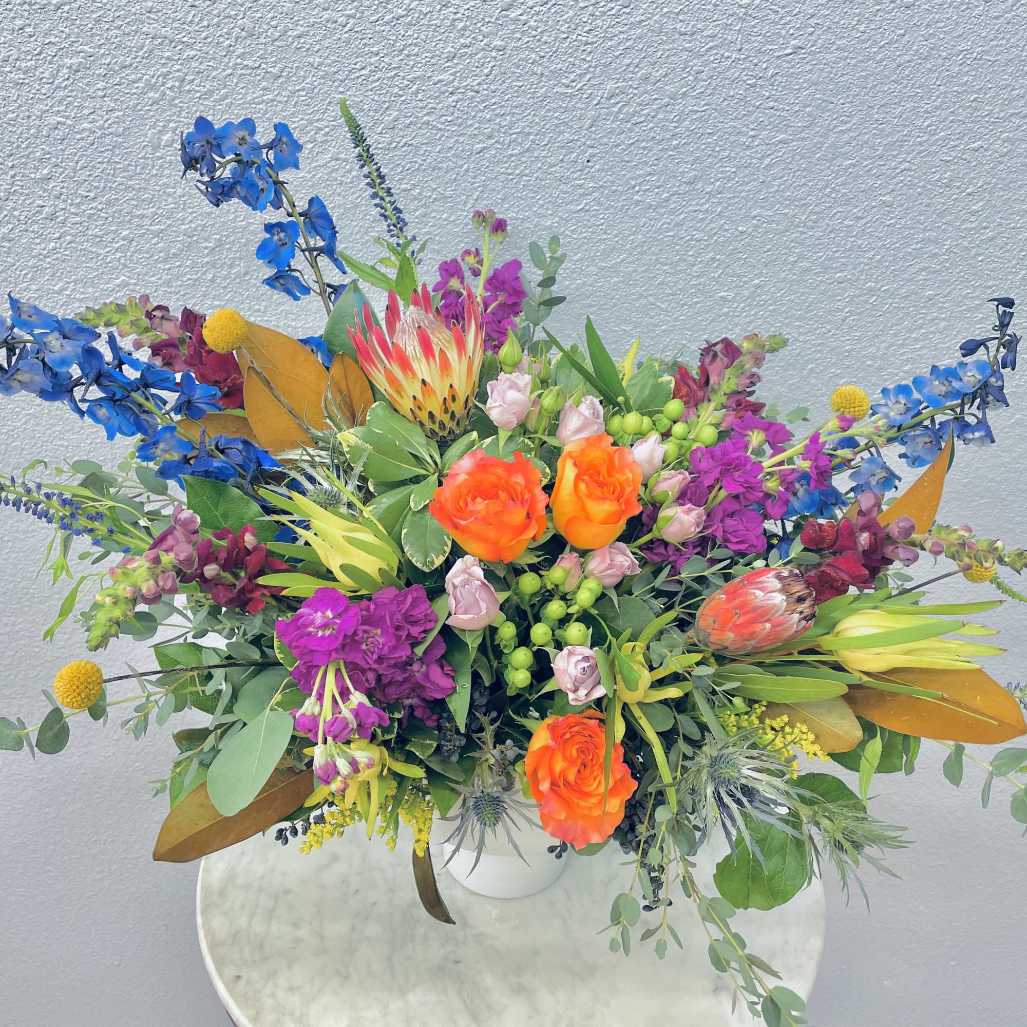 Bright mixed bouquet with orange roses, blue flowers, and pink blooms in a white vase