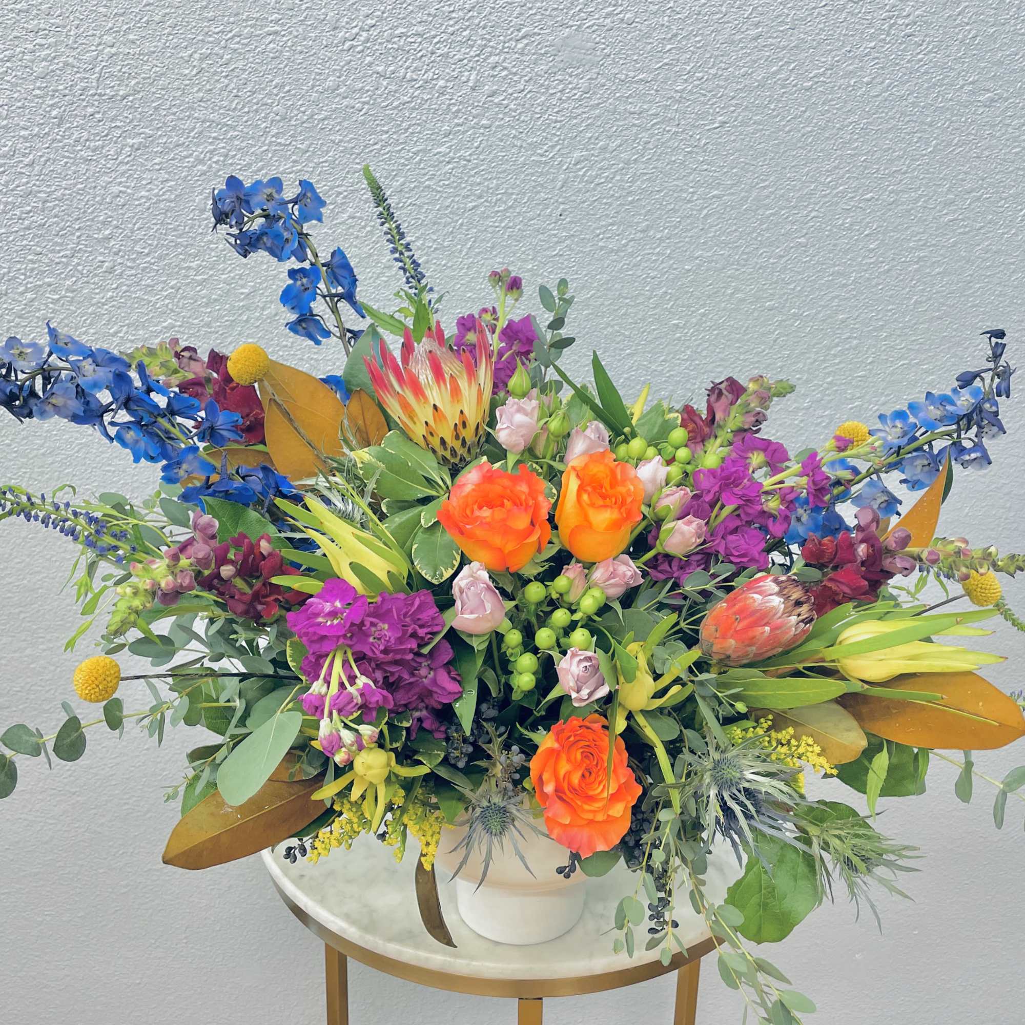 Bright mixed bouquet with orange roses and blue flowers in a white vase