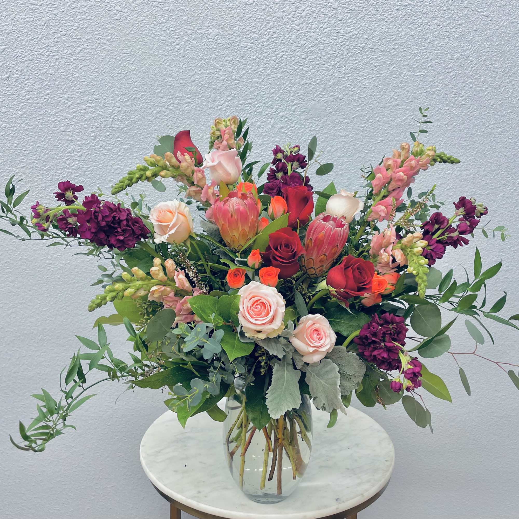 Mixed bouquet of pink, red, and purple flowers in a clear glass vase
