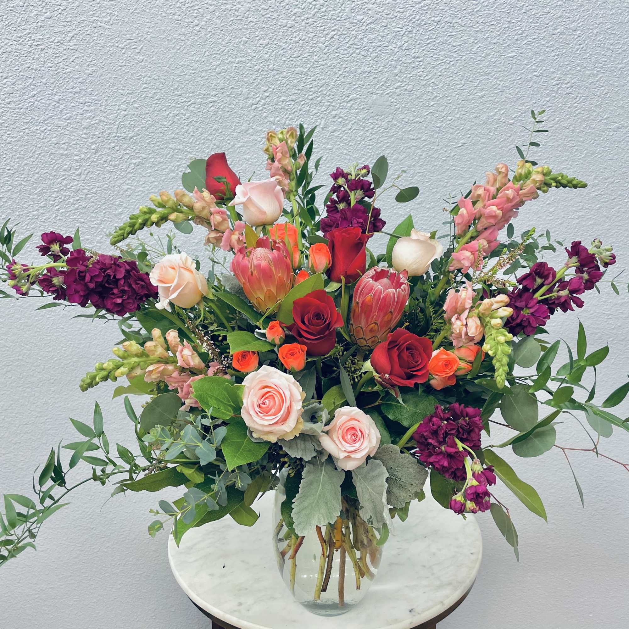 Mixed bouquet of roses, protea, and snapdragons in a clear glass vase