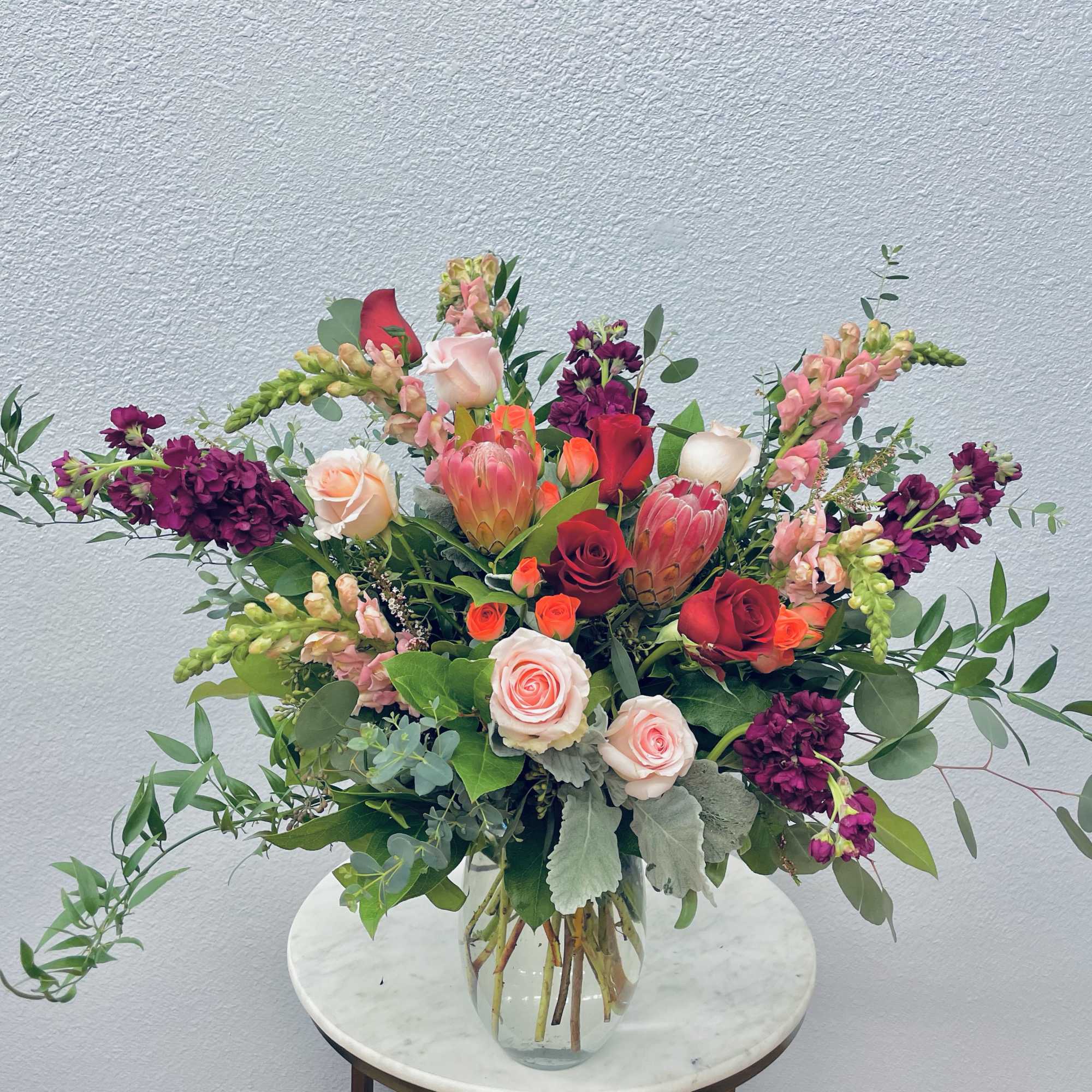Mixed bouquet of roses, protea, and snapdragons in a glass vase