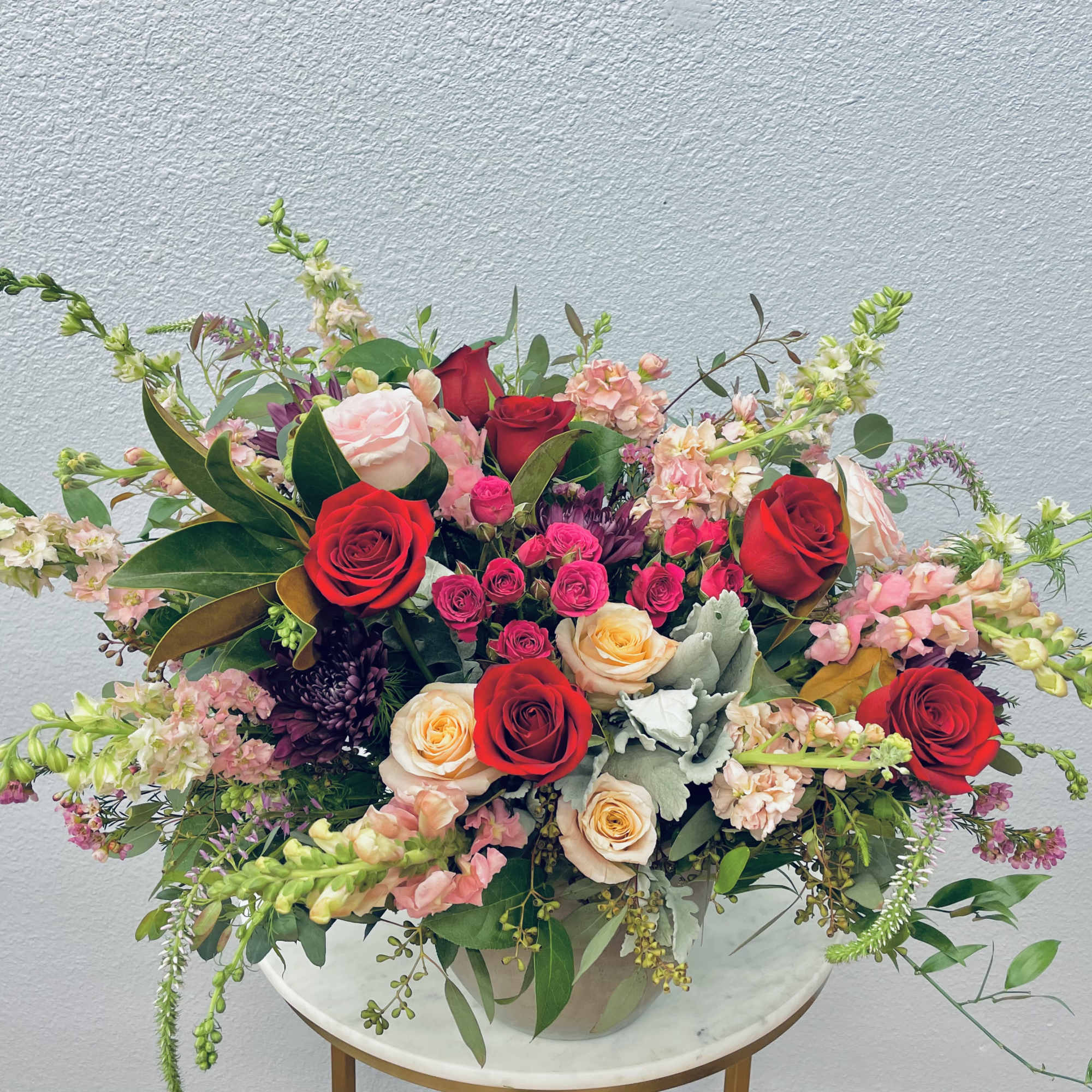 Mixed bouquet of red, pink, and peach roses in a white vase