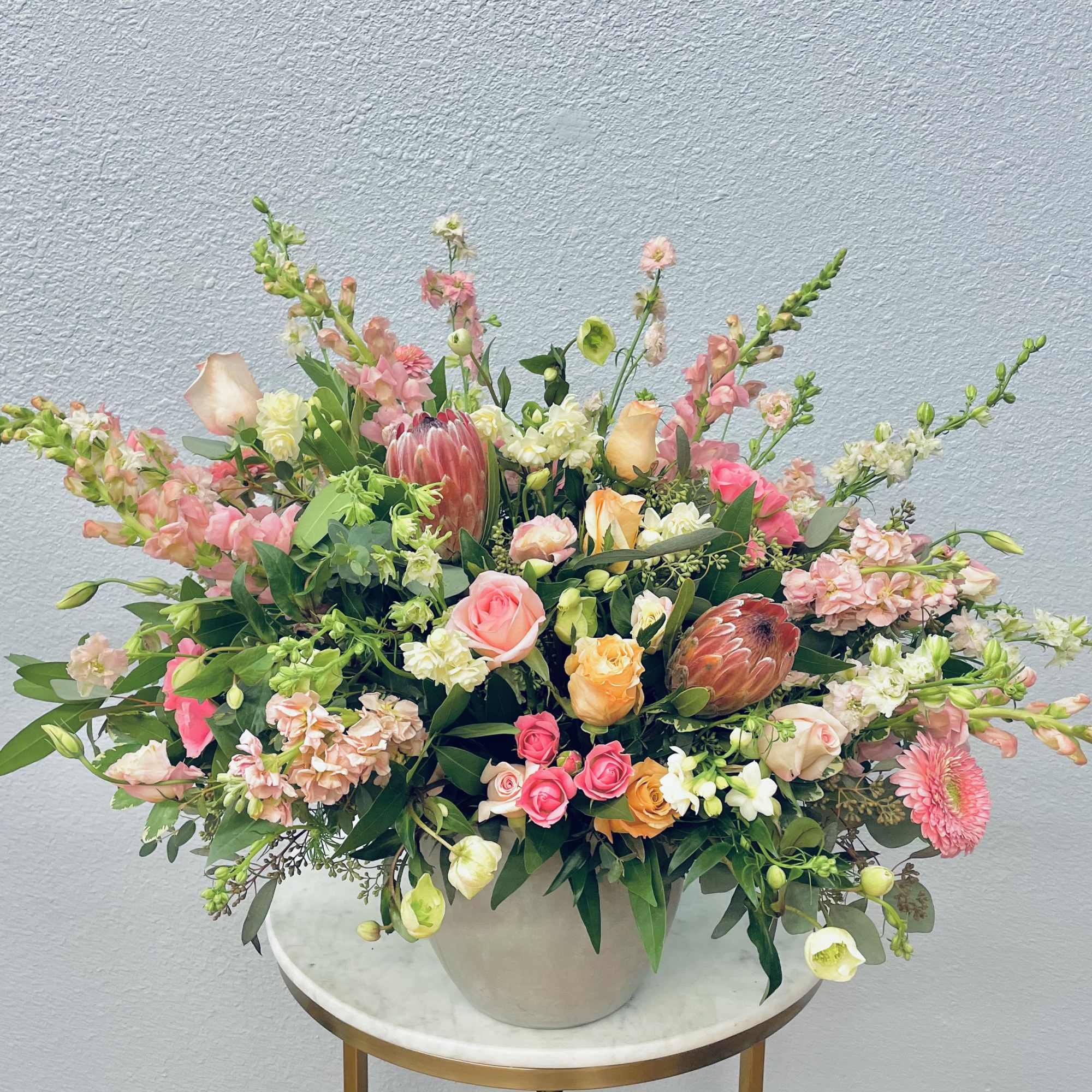 Large mixed floral arrangement in a white vase with pink, peach, and white blooms