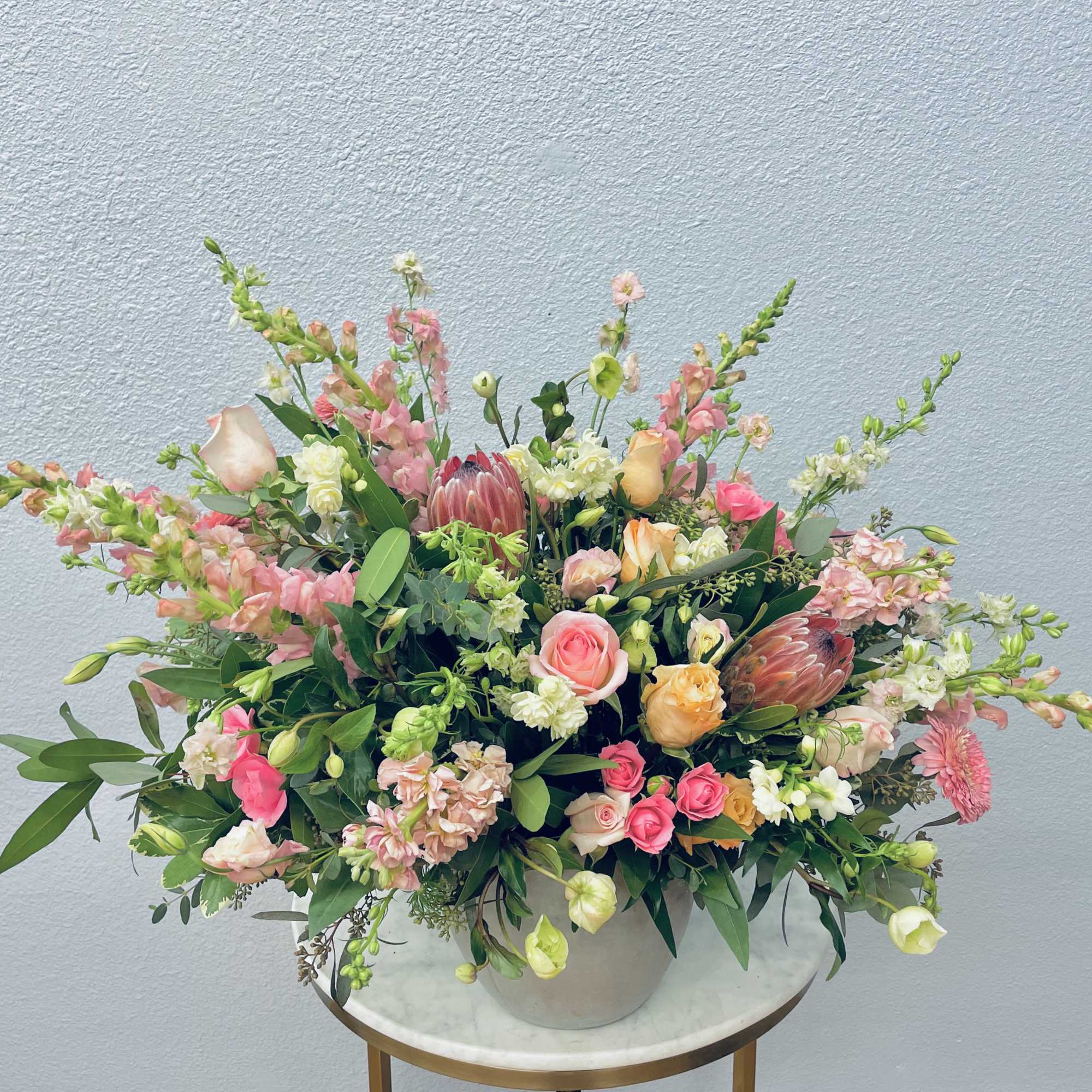 Large pastel floral arrangement in a white vase with pink and peach blooms