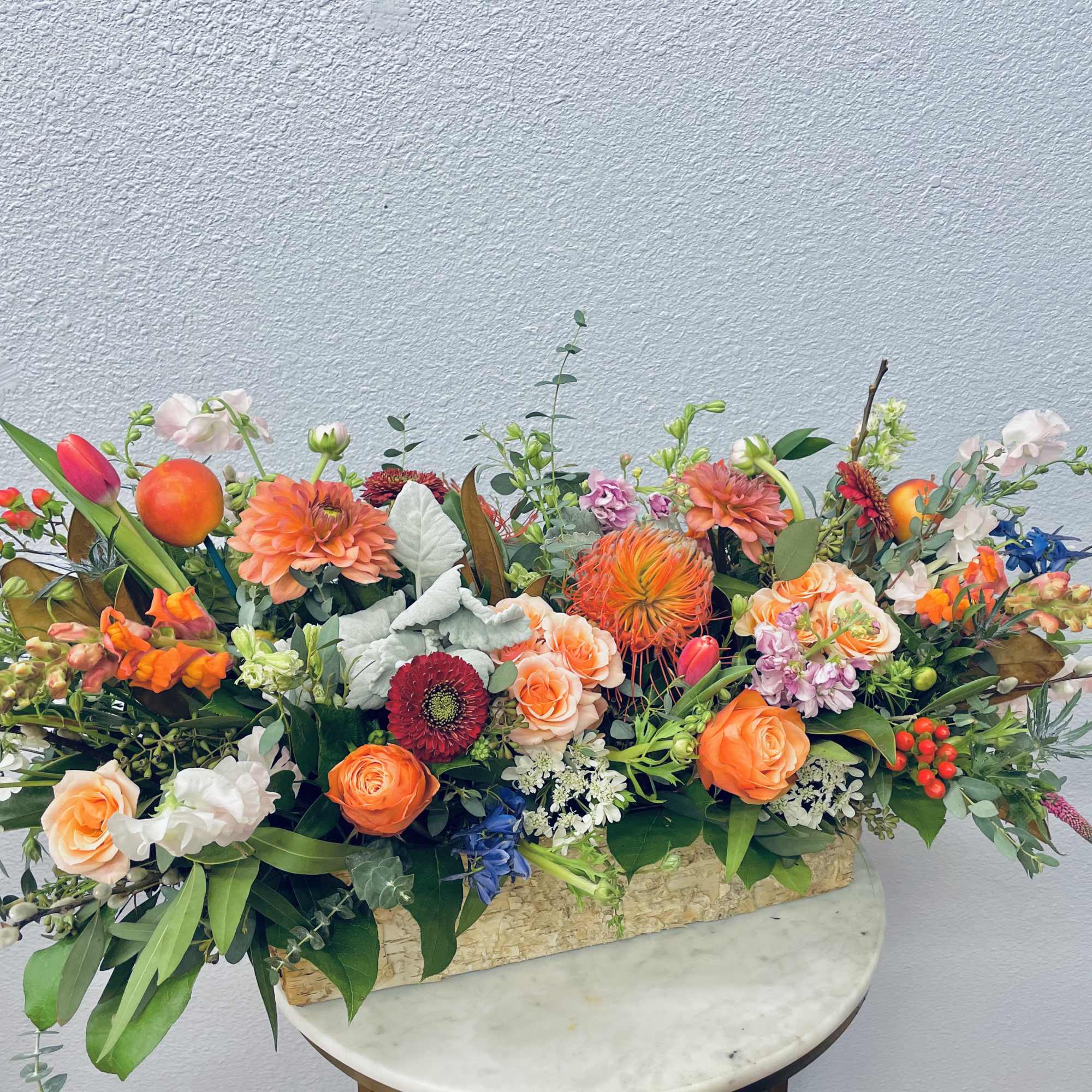 Low floral centerpiece with orange, pink, blue, and white blooms in a rectangular container