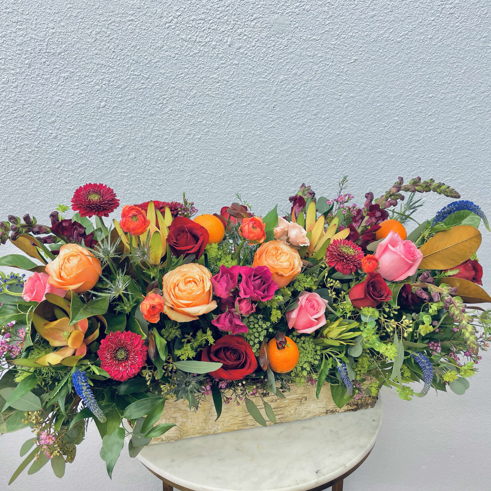 Long floral arrangement with roses and bright mixed blooms in a rustic container