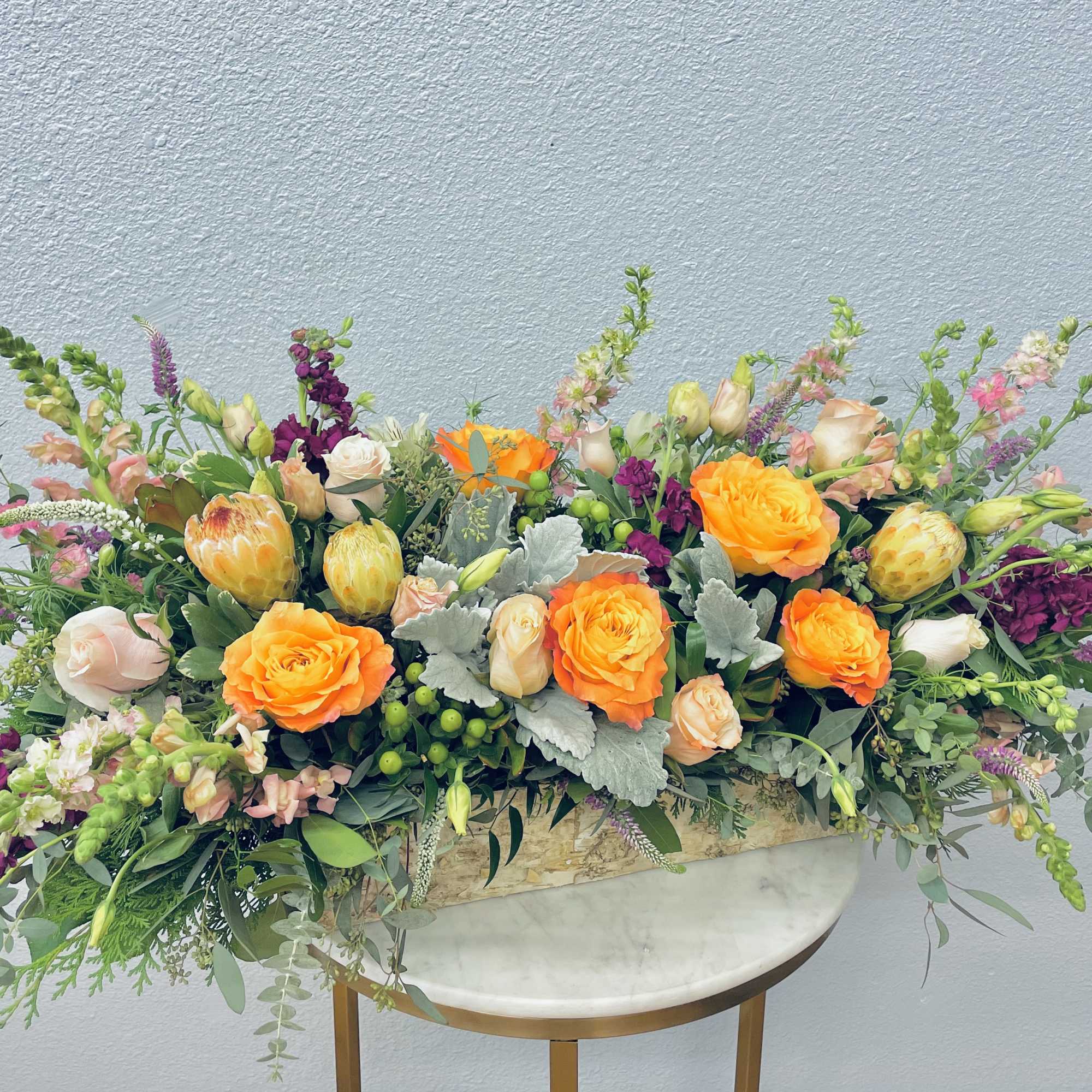 Long floral arrangement with orange roses and mixed blooms in a low container
