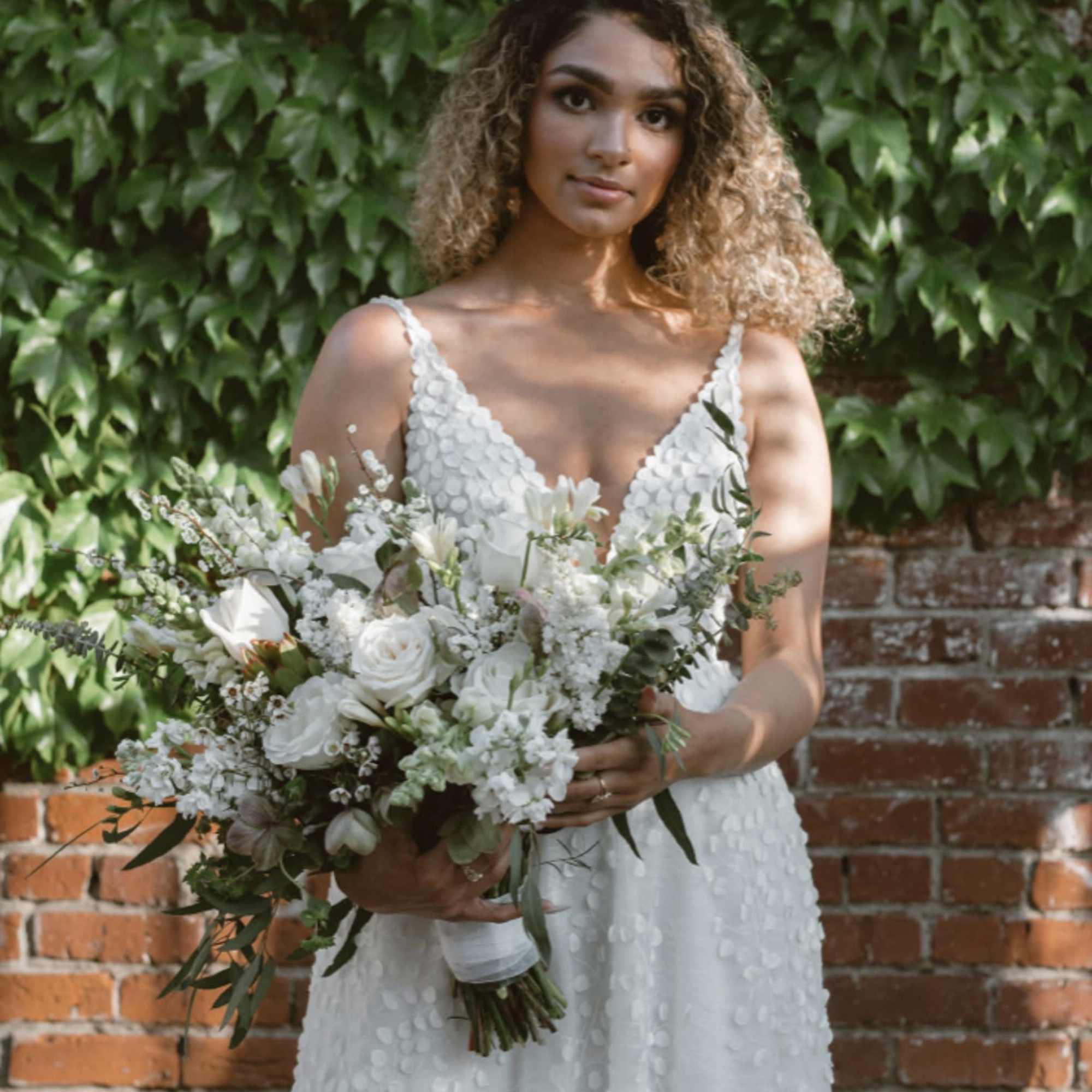 Bride holding a white bouquet in front of a brick wall