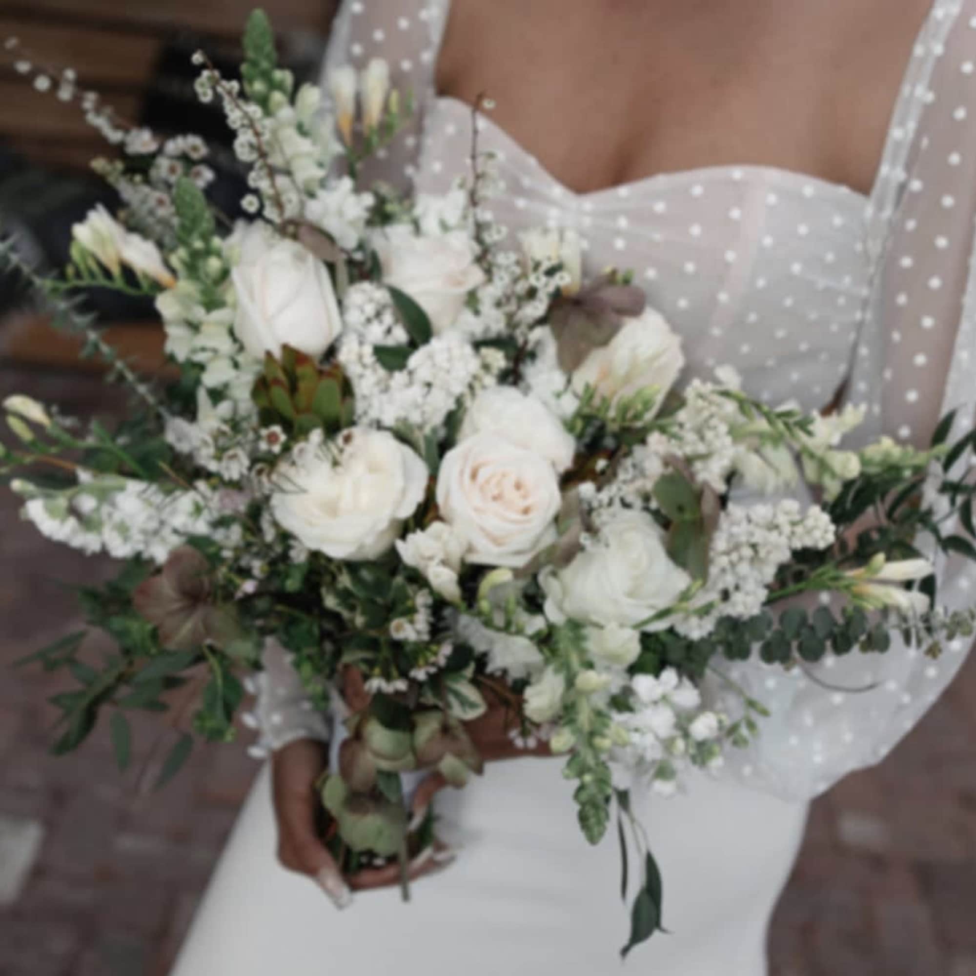 Bride holding a white bouquet with roses and greenery