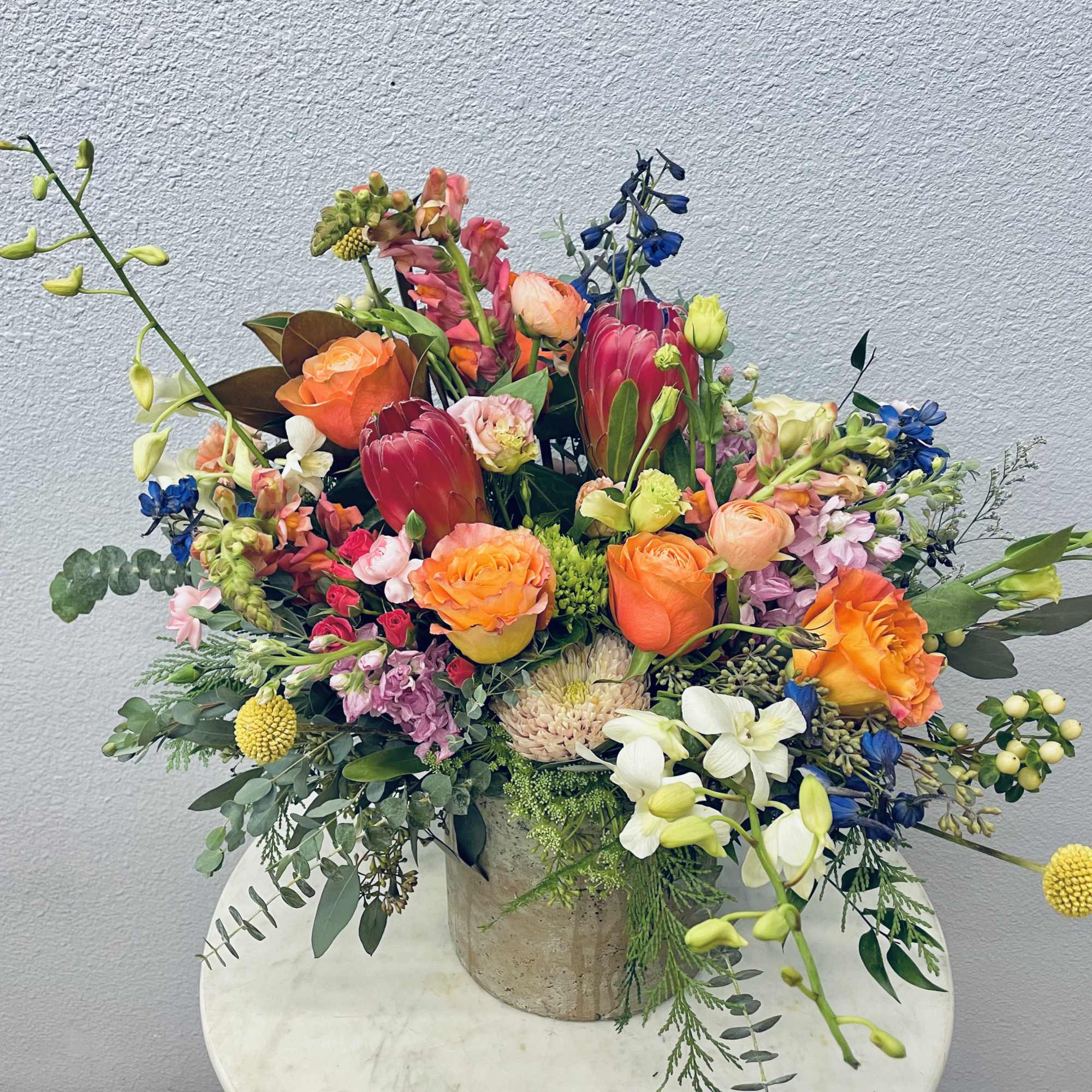Mixed bouquet in a stone vase with orange, pink, white, and blue flowers