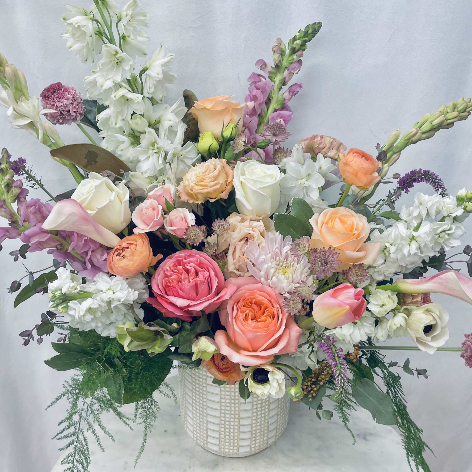 Mixed bouquet of roses, calla lilies, and snapdragons in a white vase