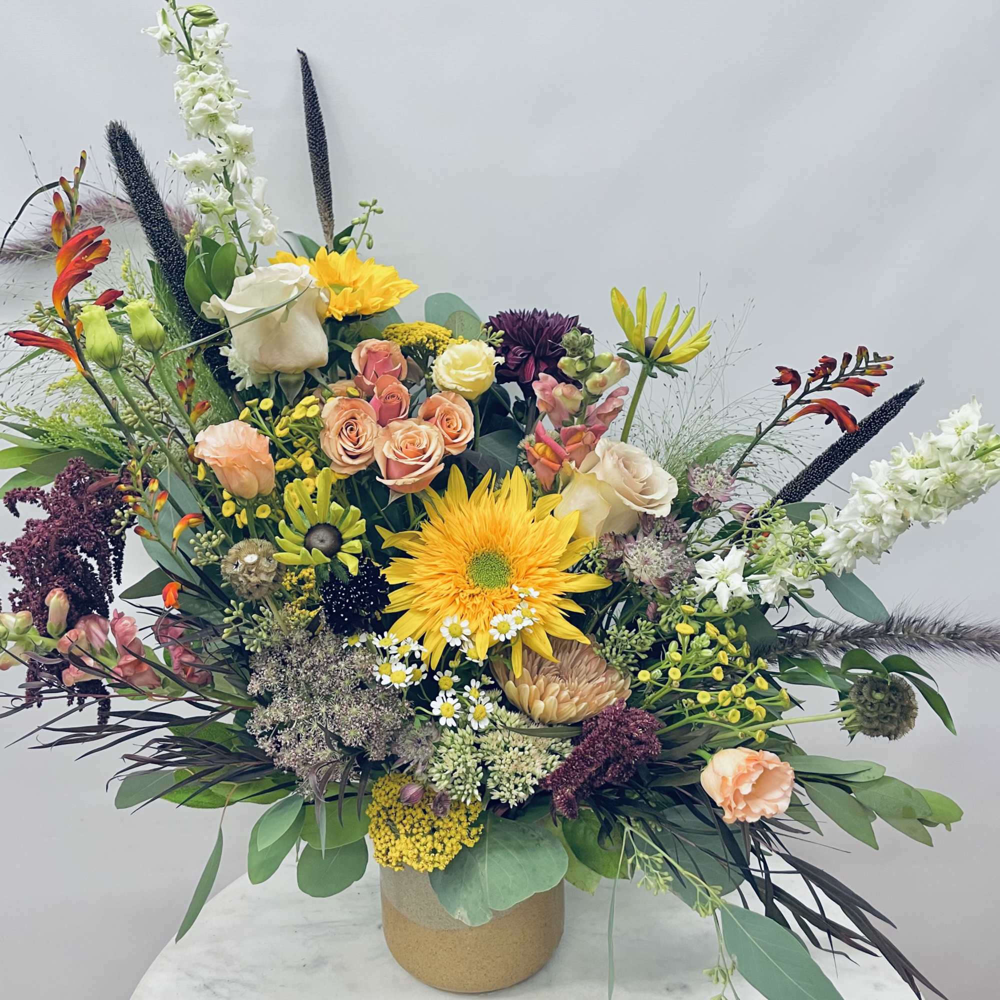 Large mixed floral arrangement in a tan vase with bright yellow and peach blooms