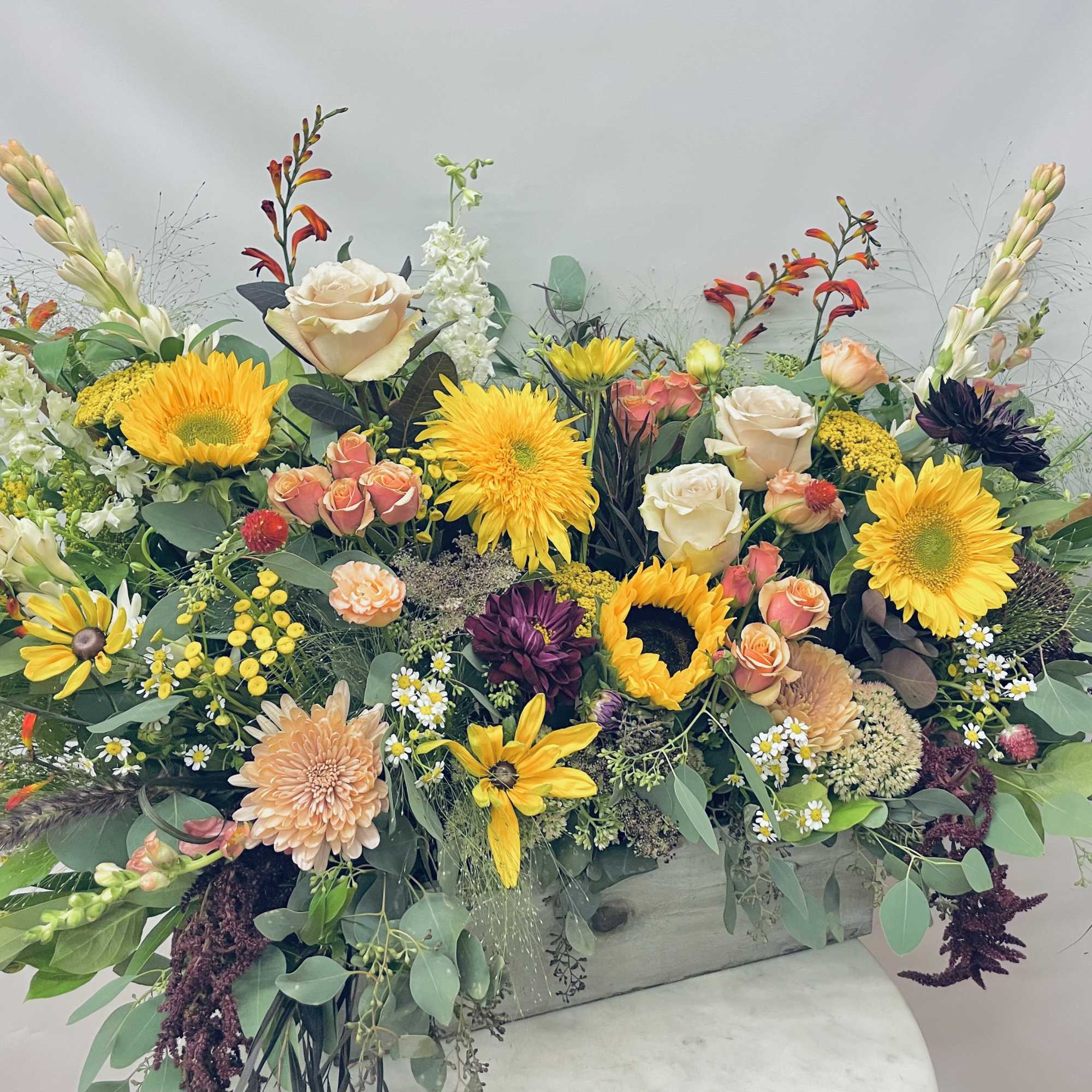 Large mixed flower arrangement with sunflowers, roses, and daisies in a rectangular container