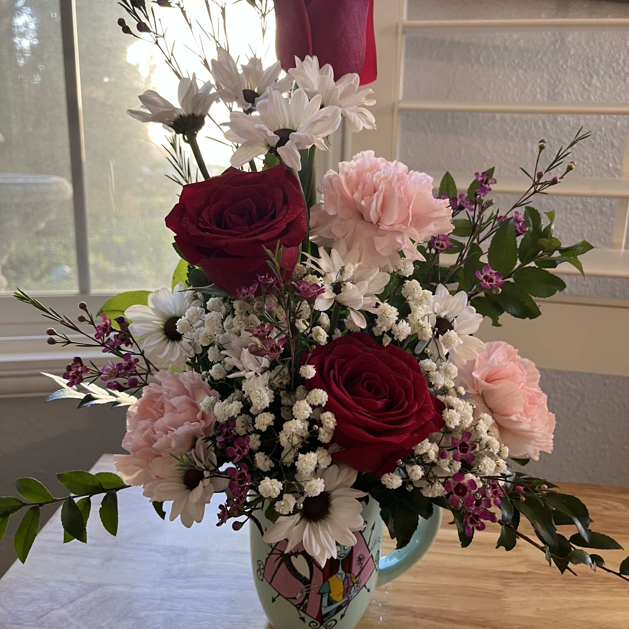 Mixed bouquet of red roses, pink carnations, and white daisies in a mug