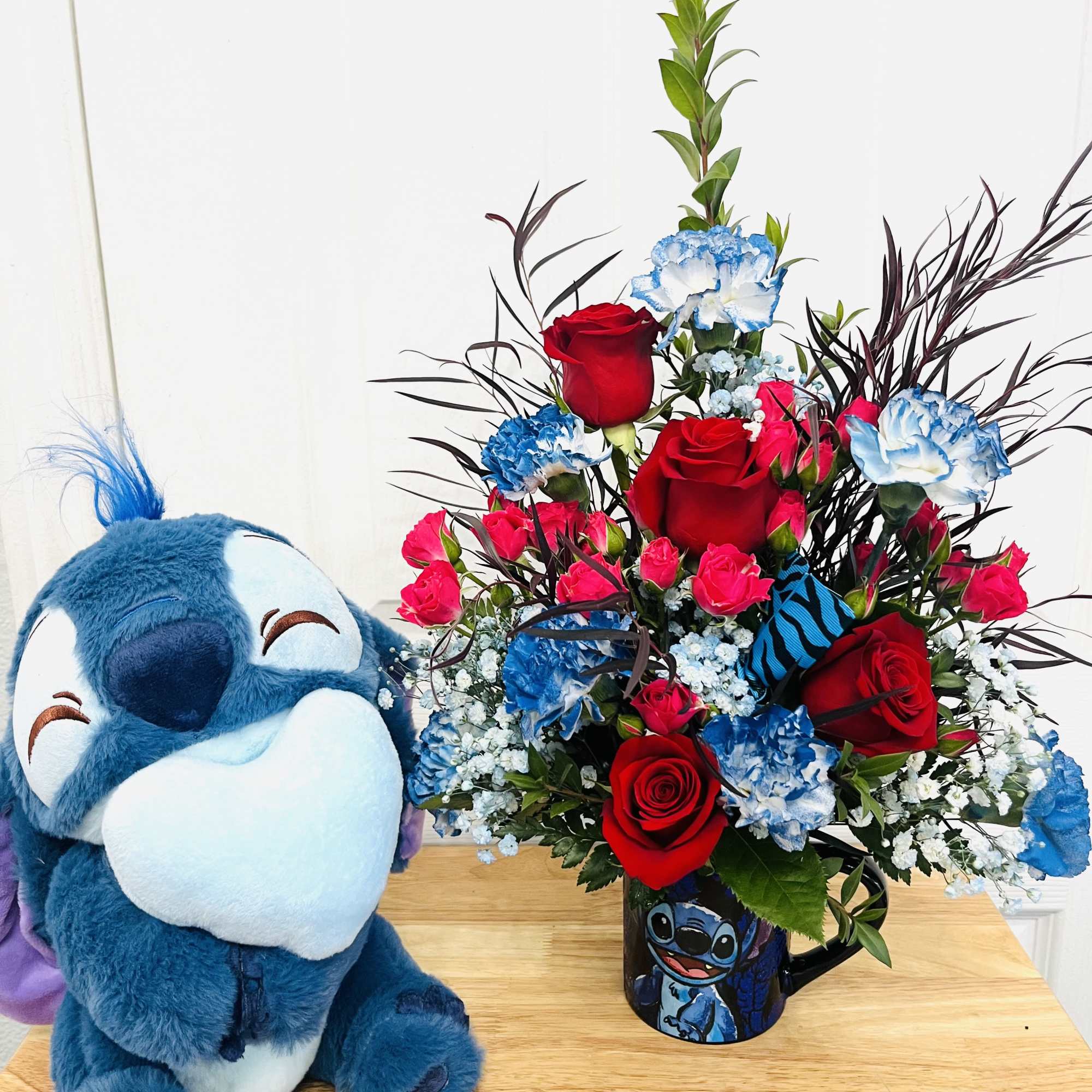 Bouquet of red roses and blue carnations in a Stitch mug beside a plush Stitch toy