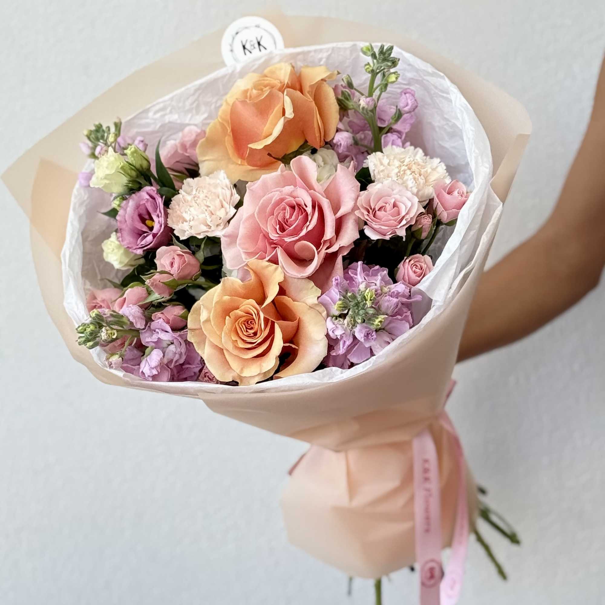 Bouquet of peach and pink roses with lavender blooms wrapped in pale paper