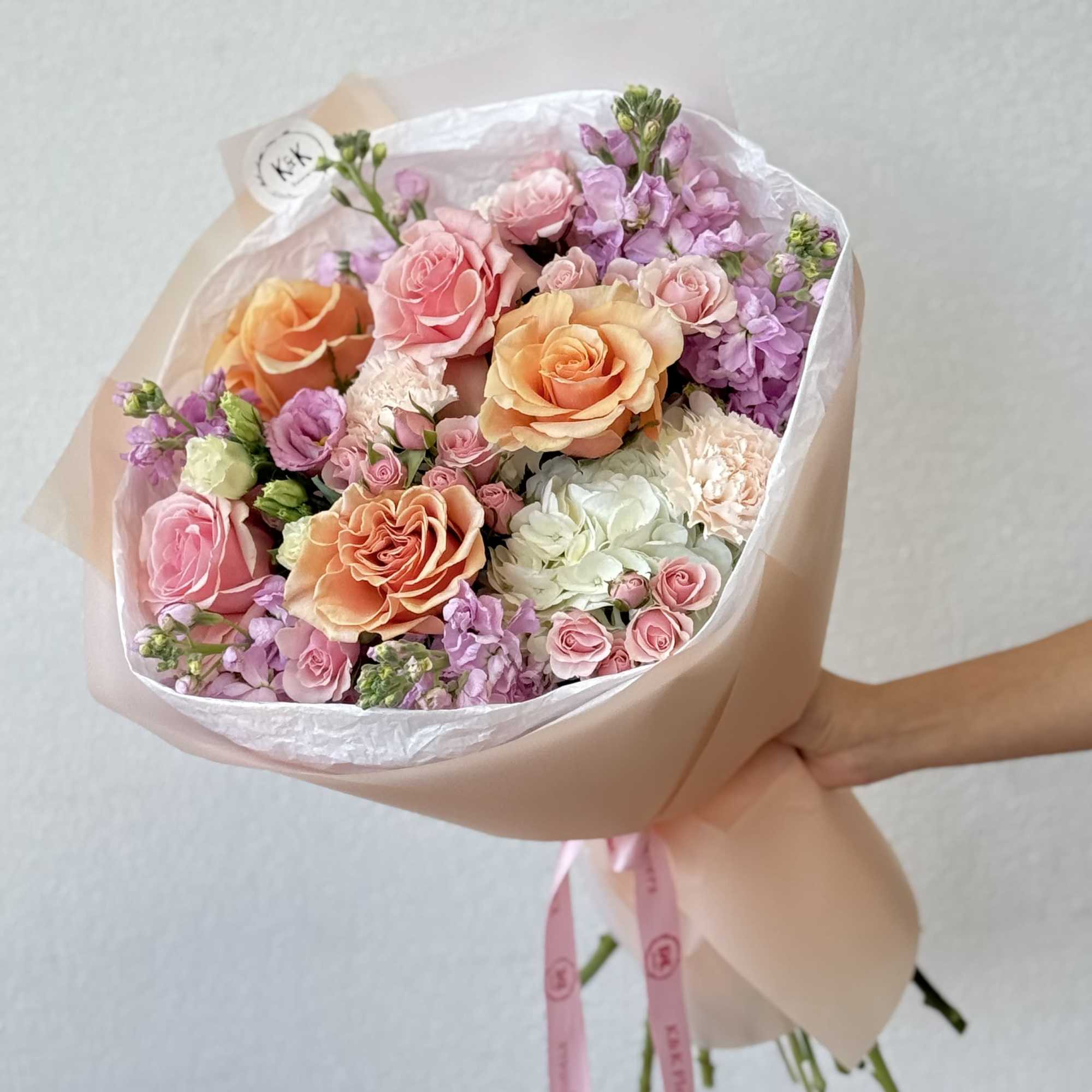 Hand-tied bouquet of pink, peach, and lavender roses with small purple blooms