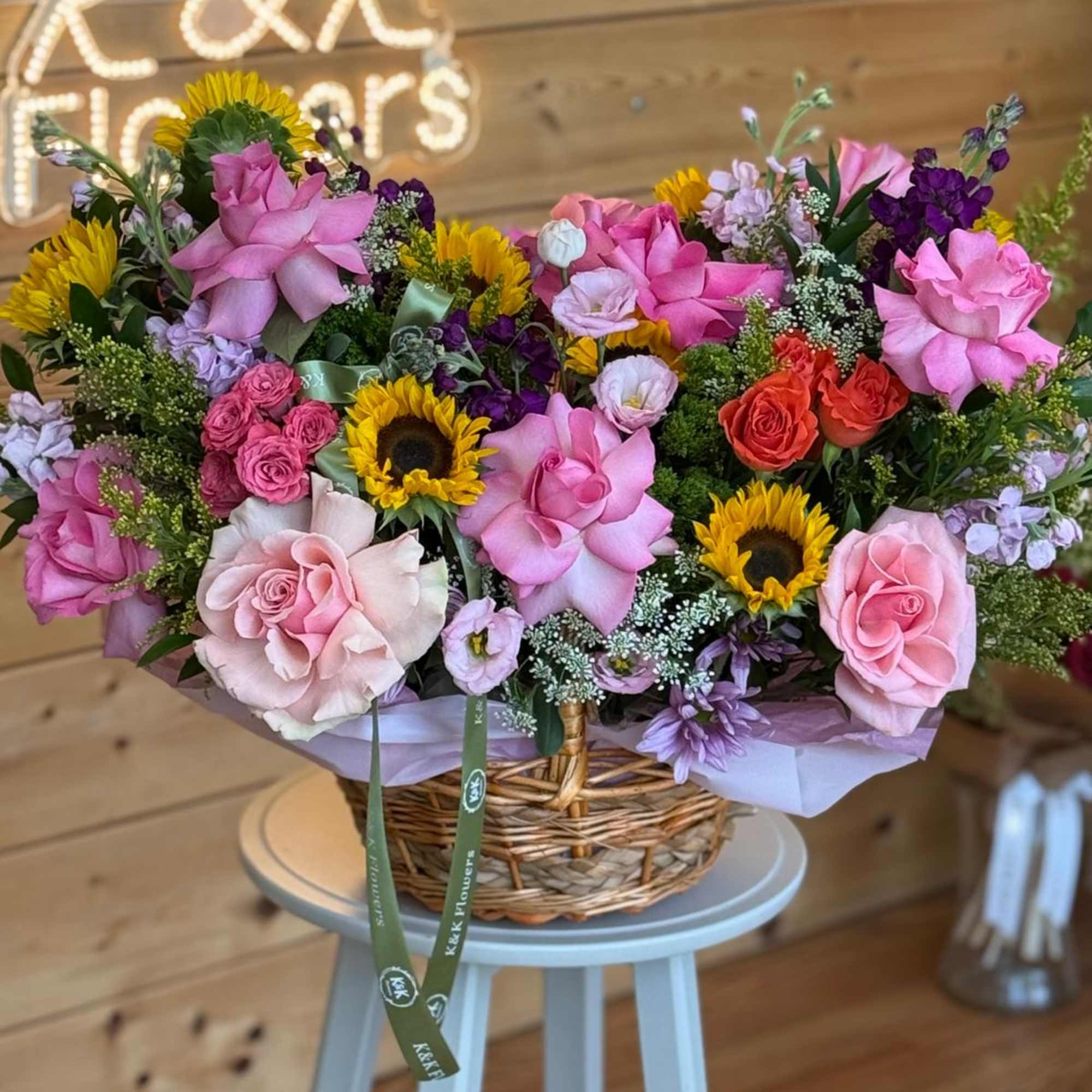 Basket arrangement of pink roses, sunflowers, and purple flowers